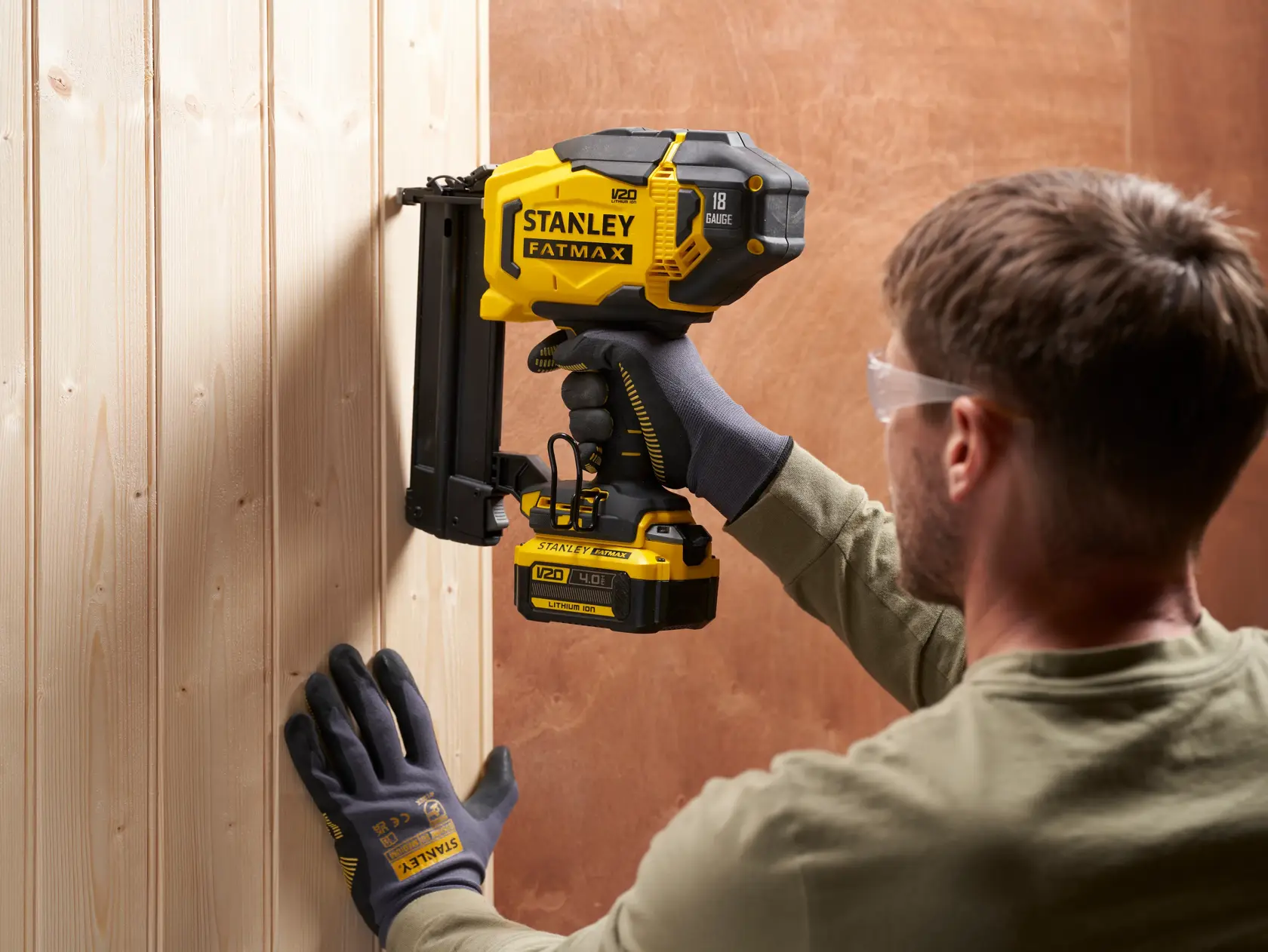 STANLEY SFMCN618B-XJ battery nailer tool used on wooden panel, side angle, yellow and black color.