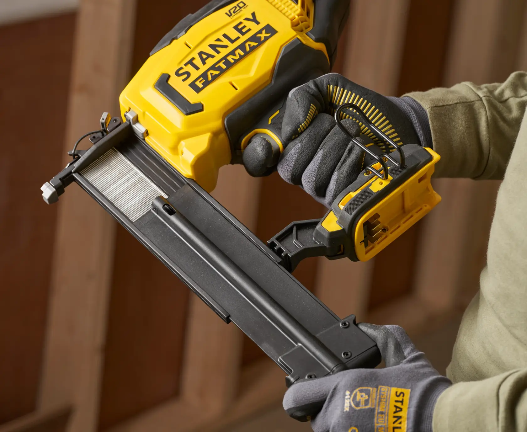 Photo of STANLEY SFMCN618B-XJ cordless nailer in use, yellow and black, shown held by gloved hands.