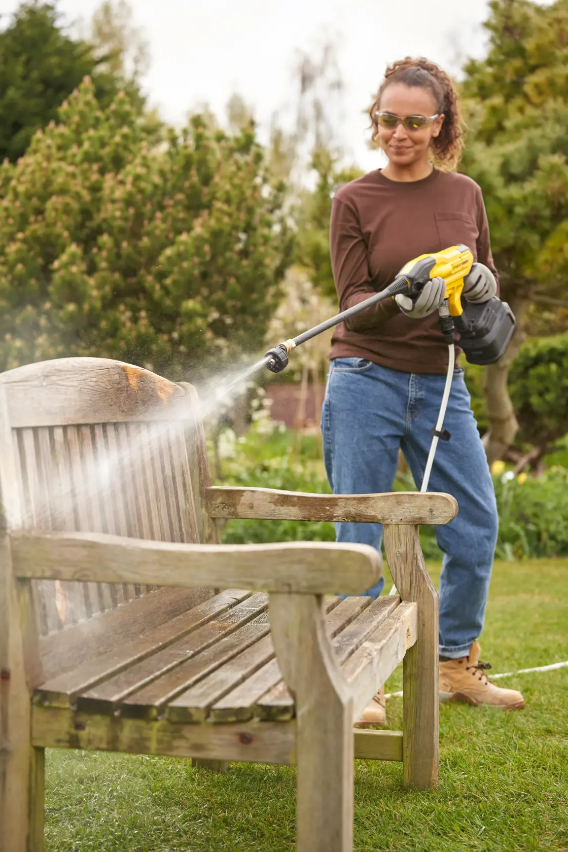 STANLEY SFMCPC93B pressure cleaner spraying water on wooden bench outdoors in garden setting.