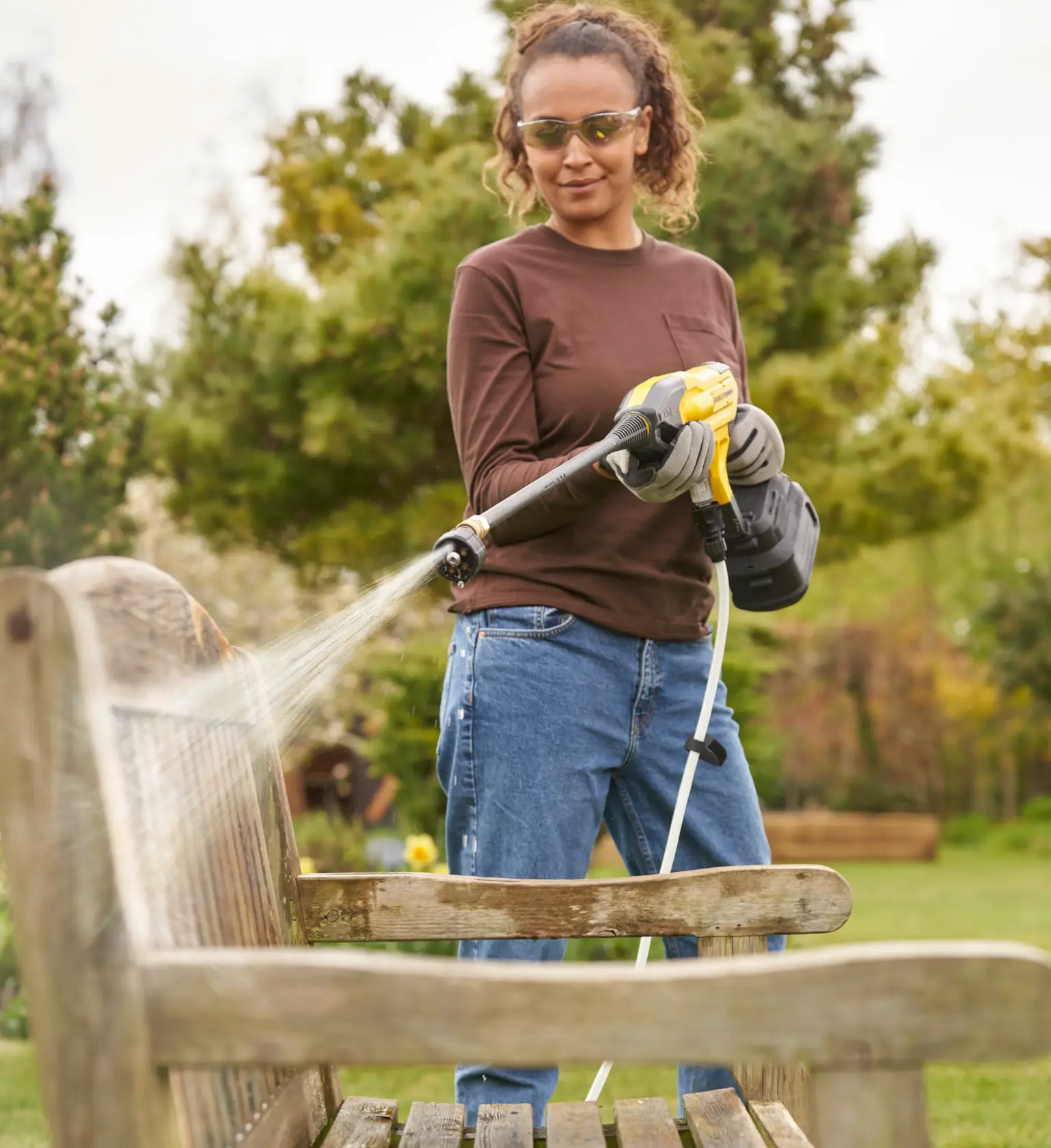 STANLEY SFMCPC93M1 portable pressure cleaner spraying water on wooden bench outdoors.