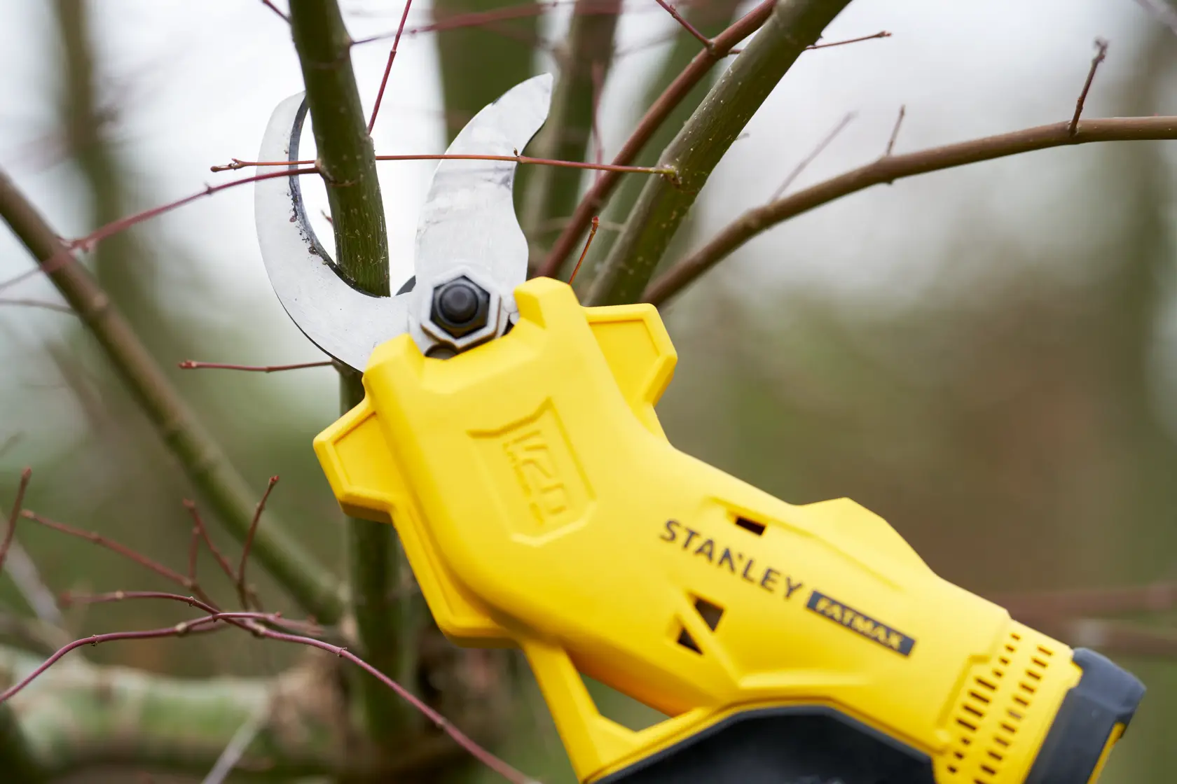 STANLEY SFMCPP32B yellow cordless pruning shear cutting a tree branch outdoors, close-up.