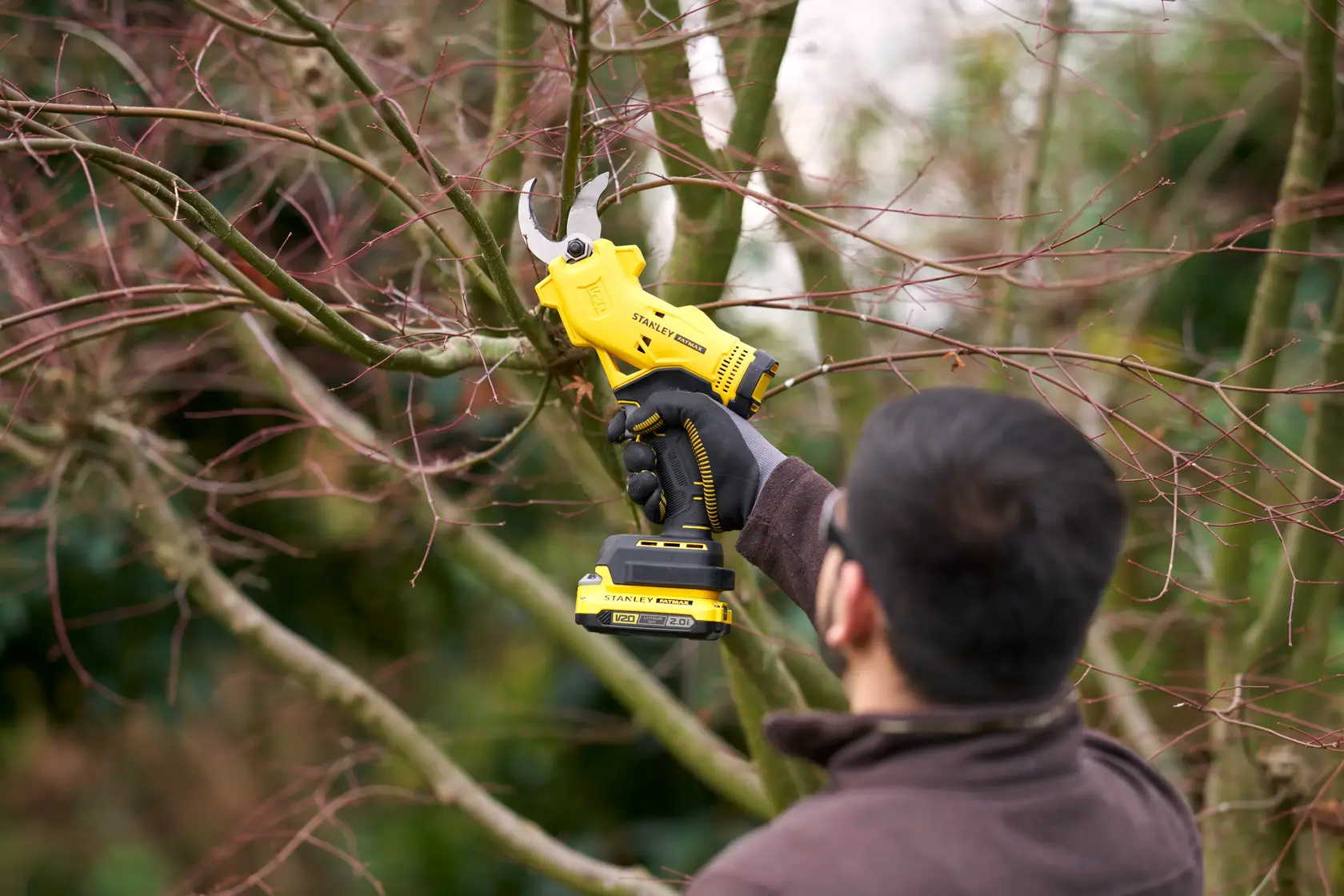 Stanley SFMCPP32D1 cordless electric pruner in use, cutting tree branches outdoors.