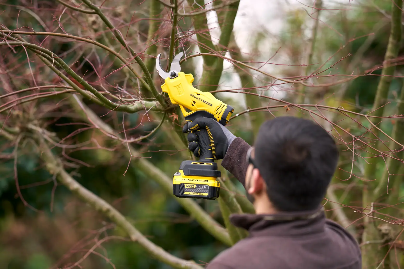 STANLEY SFMCPP32M1 cordless pruning shears in use cutting tree branches outdoors.