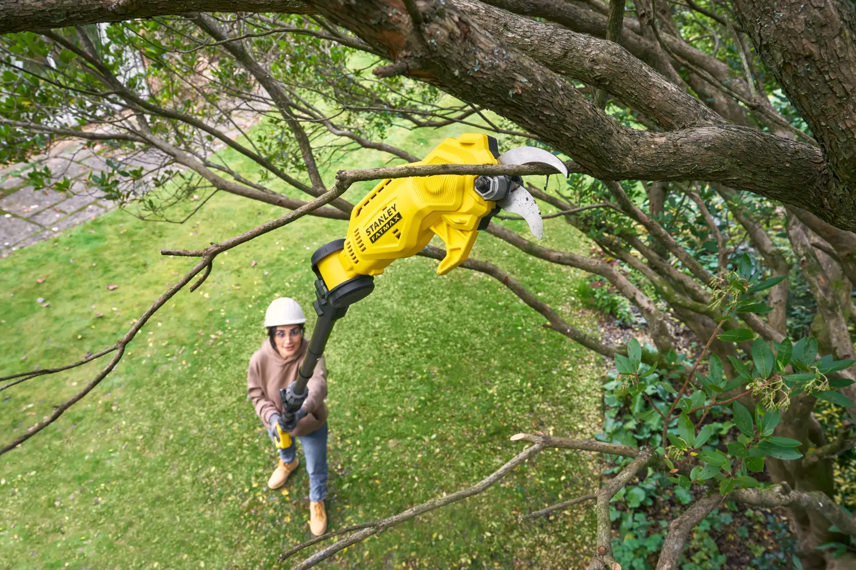 Photo of STANLEY SFMCPP632B pole pruner cutting tree branch outdoors, person using tool from ground.
