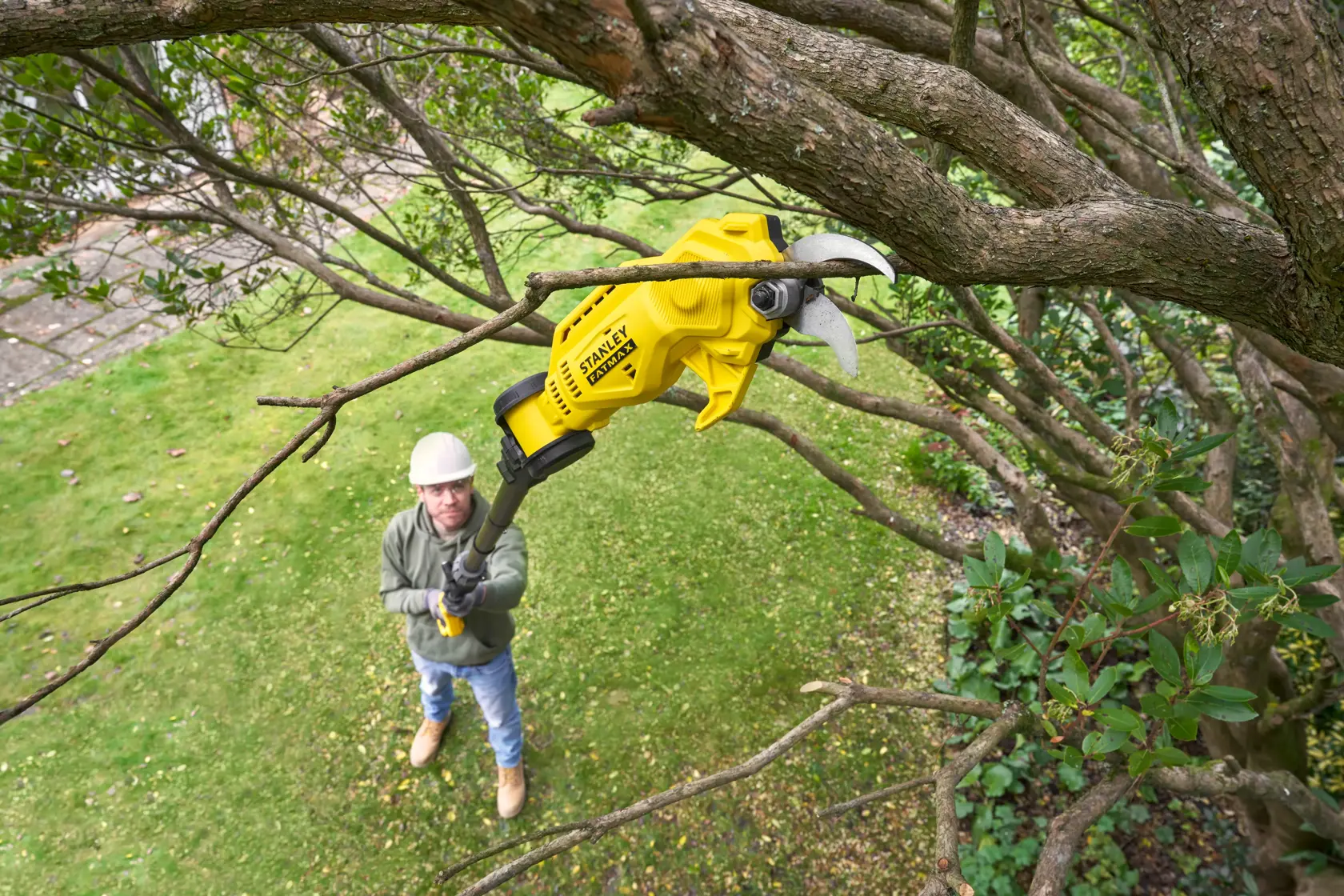 STANLEY SFMCPP632B pole pruner trimming tree branches outdoors, yellow body, garden setting.
