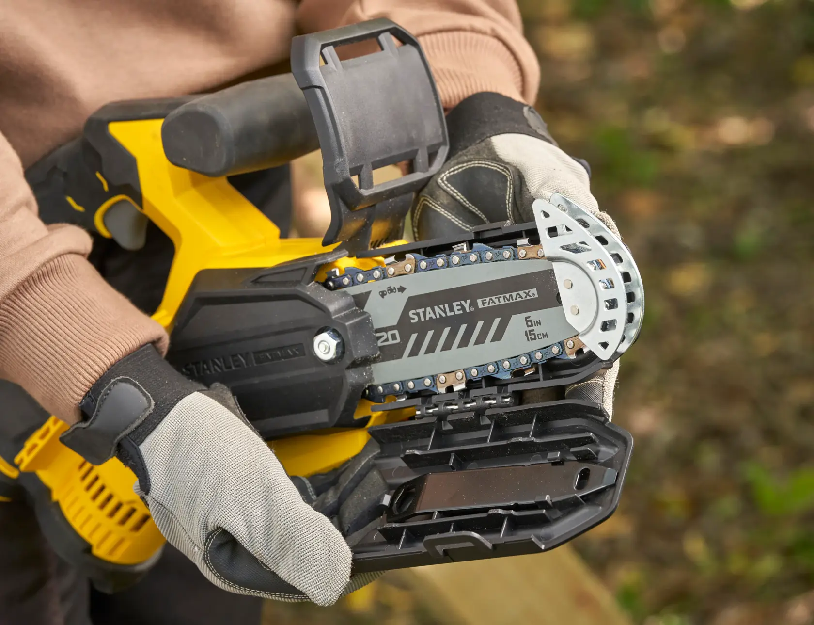 STANLEY SFMCPS415D1 FatMax chainsaw close-up, showing chain bar and protective gloves outdoors.