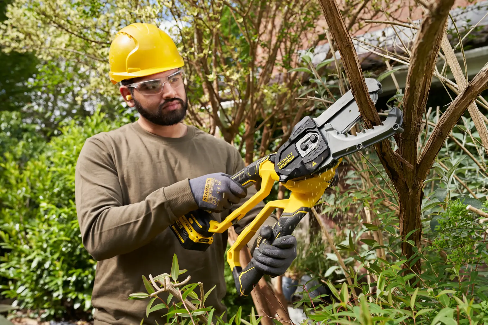 STANLEY SFMCPS515B cordless pruner saw in use, cutting tree branches outdoors.