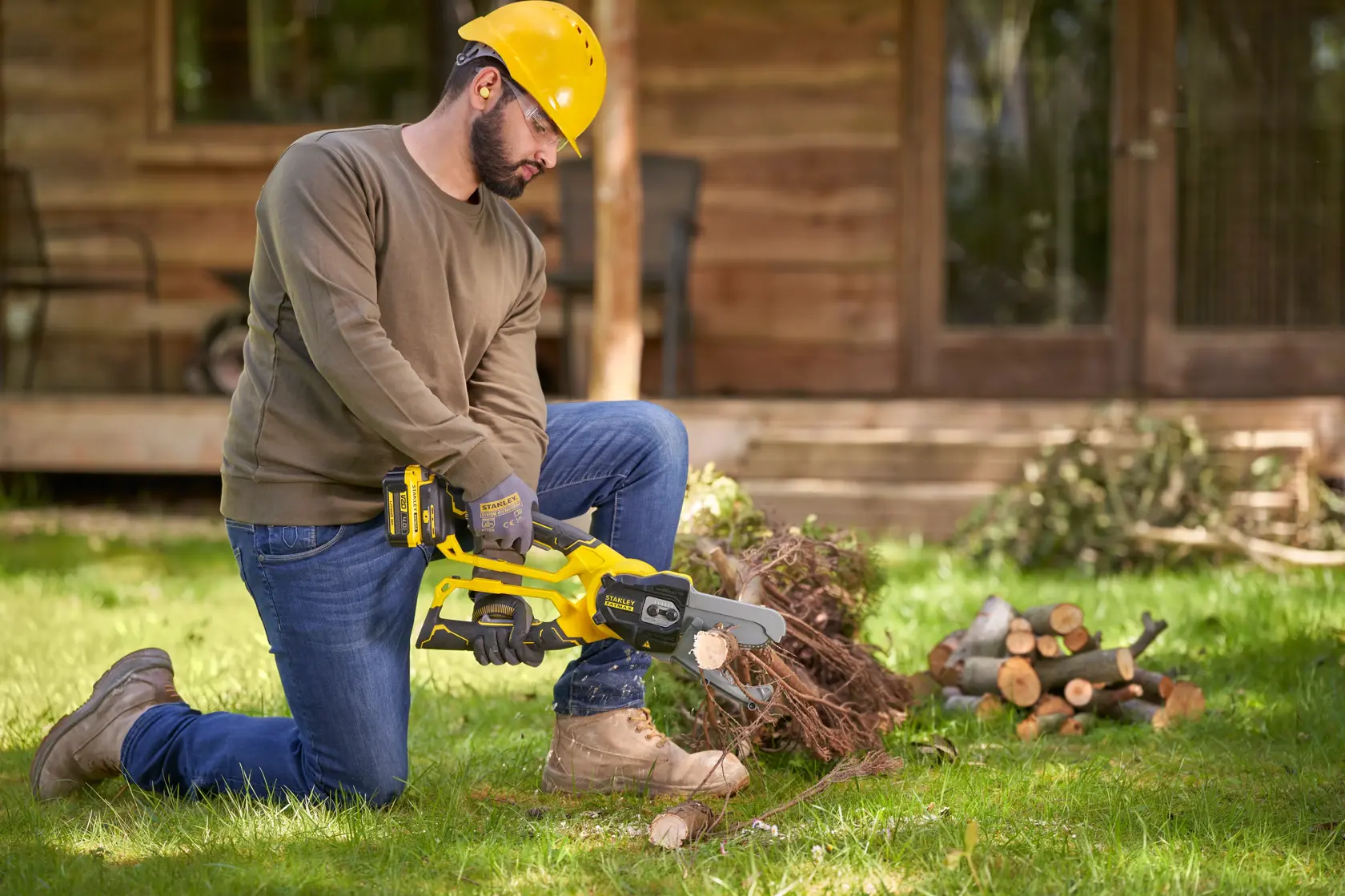 Photo of STANLEY SFMCPS515M1 cordless chainsaw in use, man cutting wood in a garden setting.