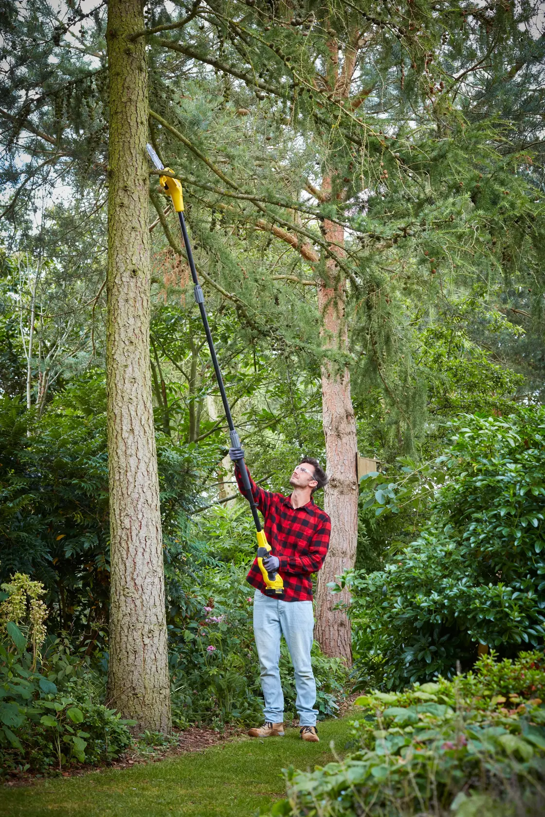 STANLEY SFMCPS620B pole saw in use trimming high tree branches in a garden.