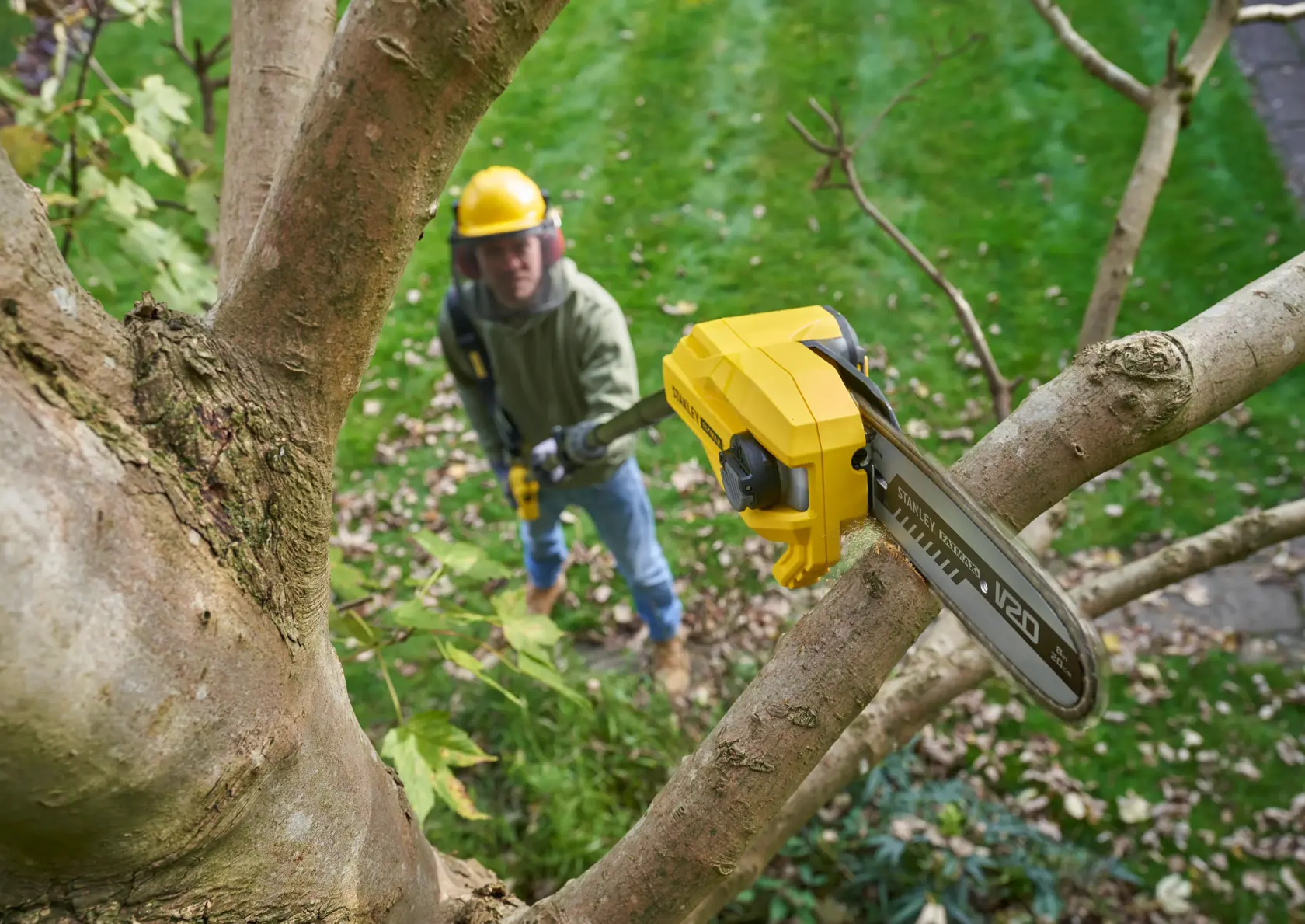 STANLEY SFMCPS720M1 pole saw trimming tree branch outdoors, close-up of saw blade cutting wood.