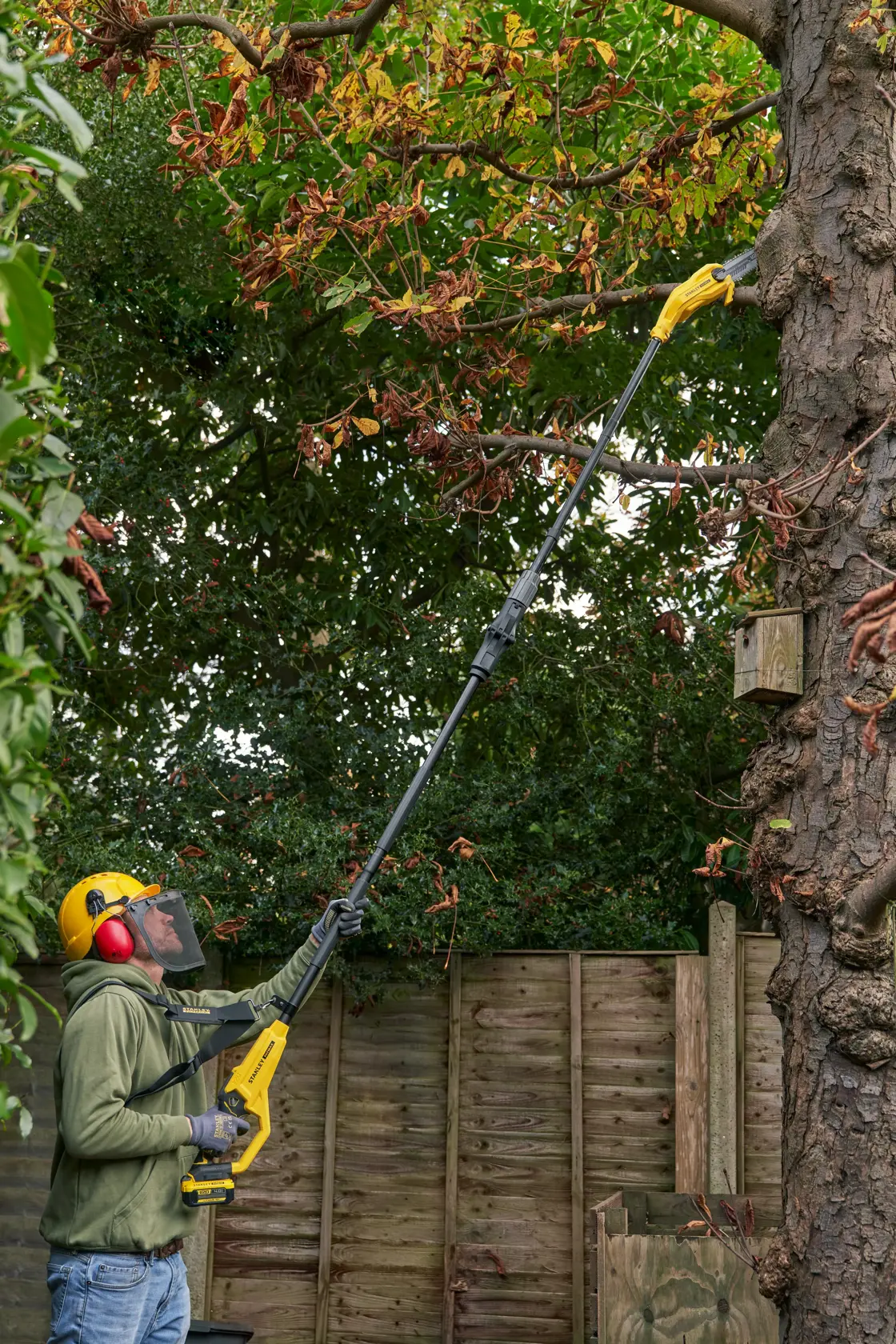 STANLEY SFMCPS720M1 pole saw used for cutting high tree branches in a garden setting.