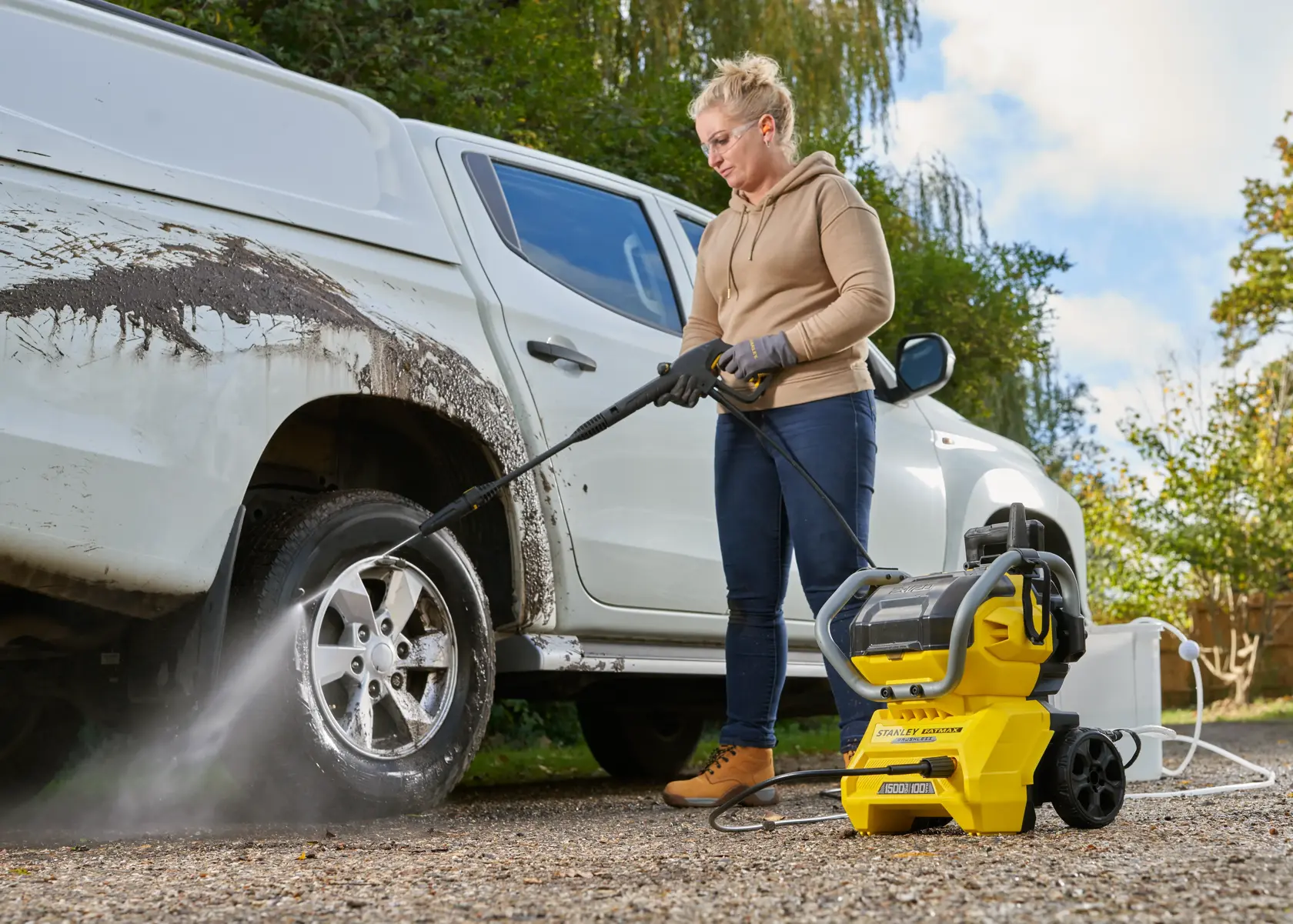 STANLEY SFMCPW1500B pressure washer cleaning a dirty white vehicle's wheel outdoors.