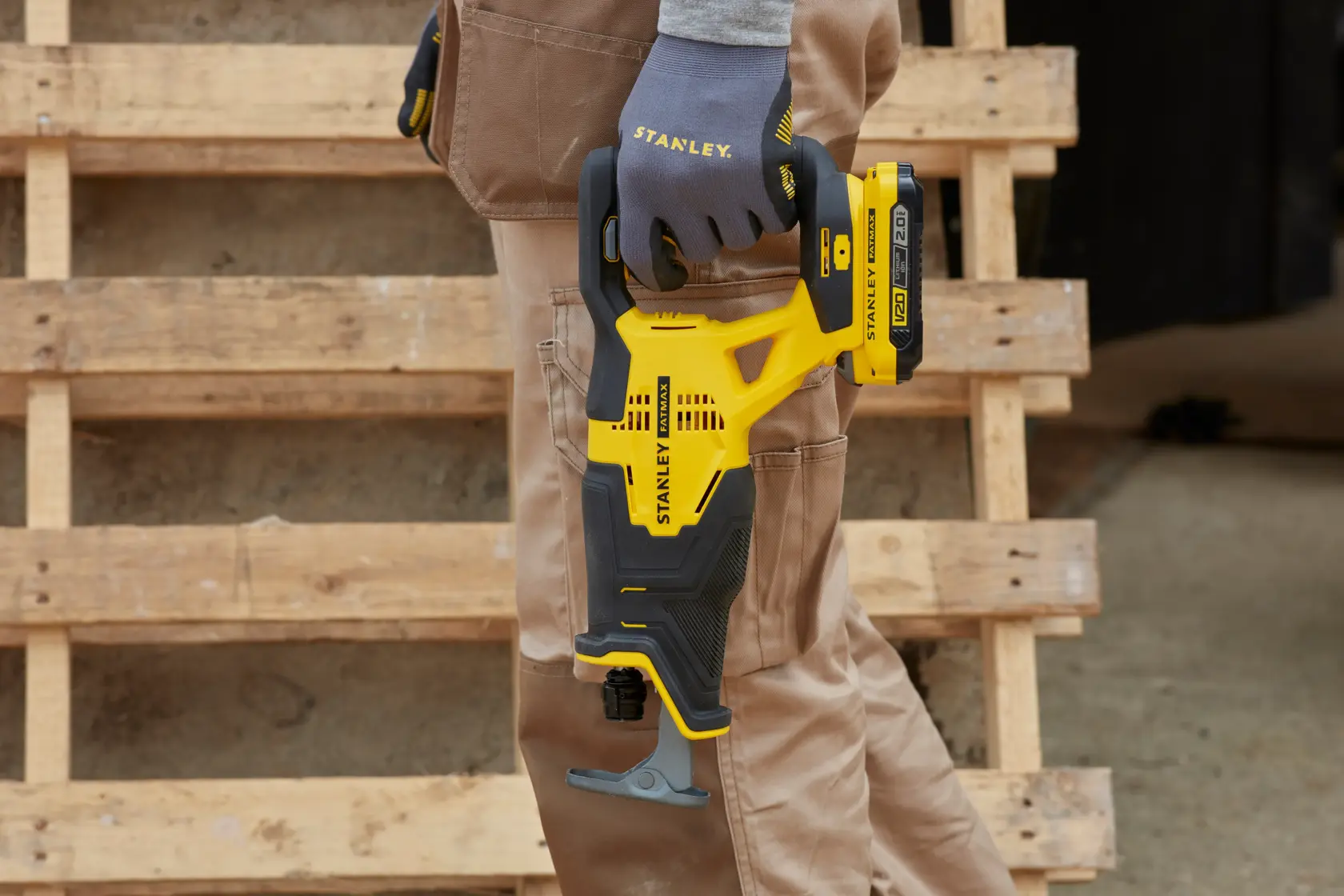 STANLEY SFMCS300B reciprocating saw held by a gloved hand, yellow and black design, construction setting.