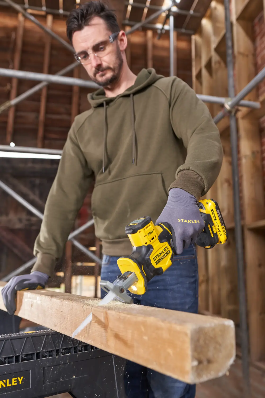 STANLEY SFMCS305B compact yellow cordless saw cutting a wooden beam, held by person wearing gloves.