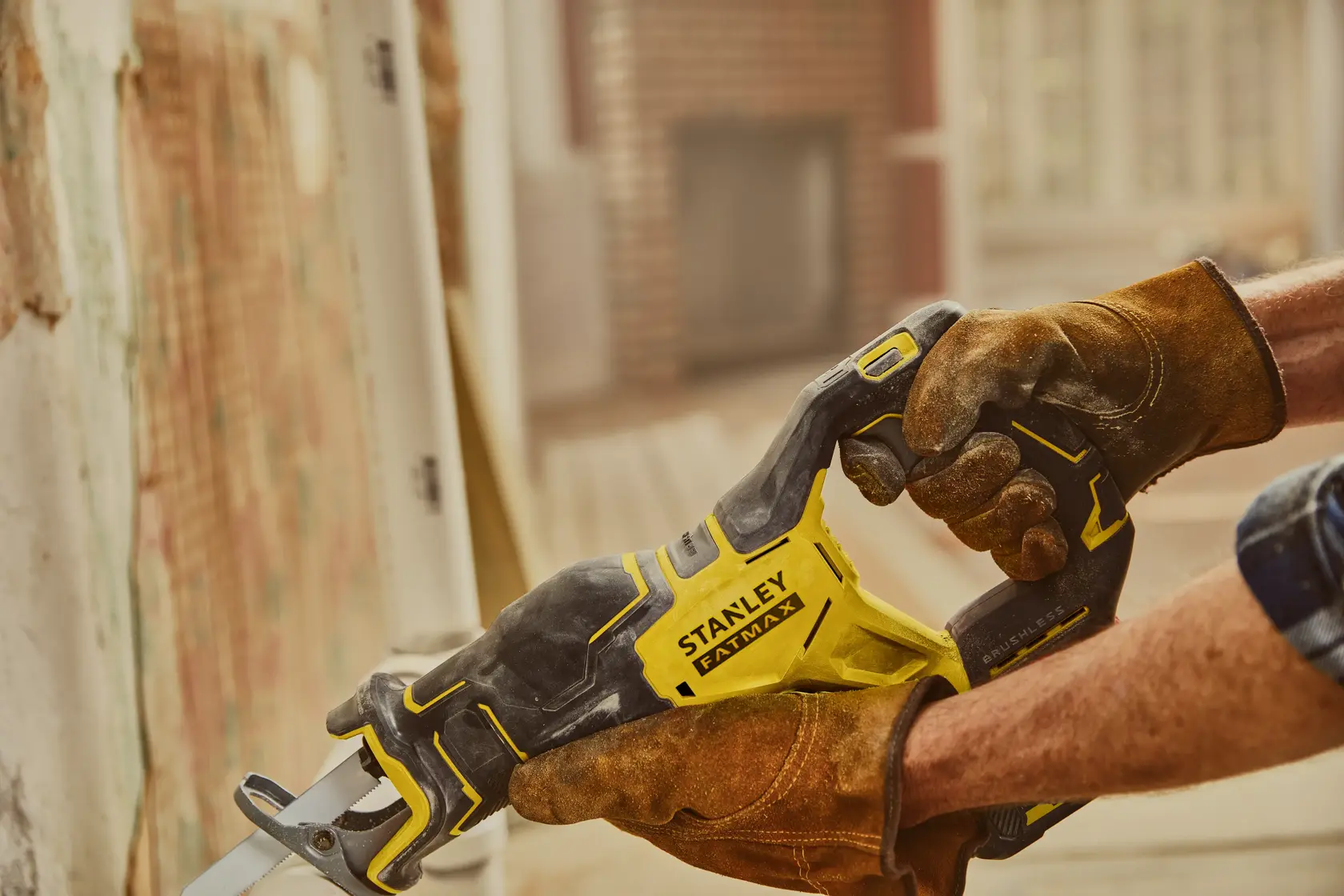 STANLEY SFMCS310B reciprocating saw with yellow and black body in use, worn work gloves visible.