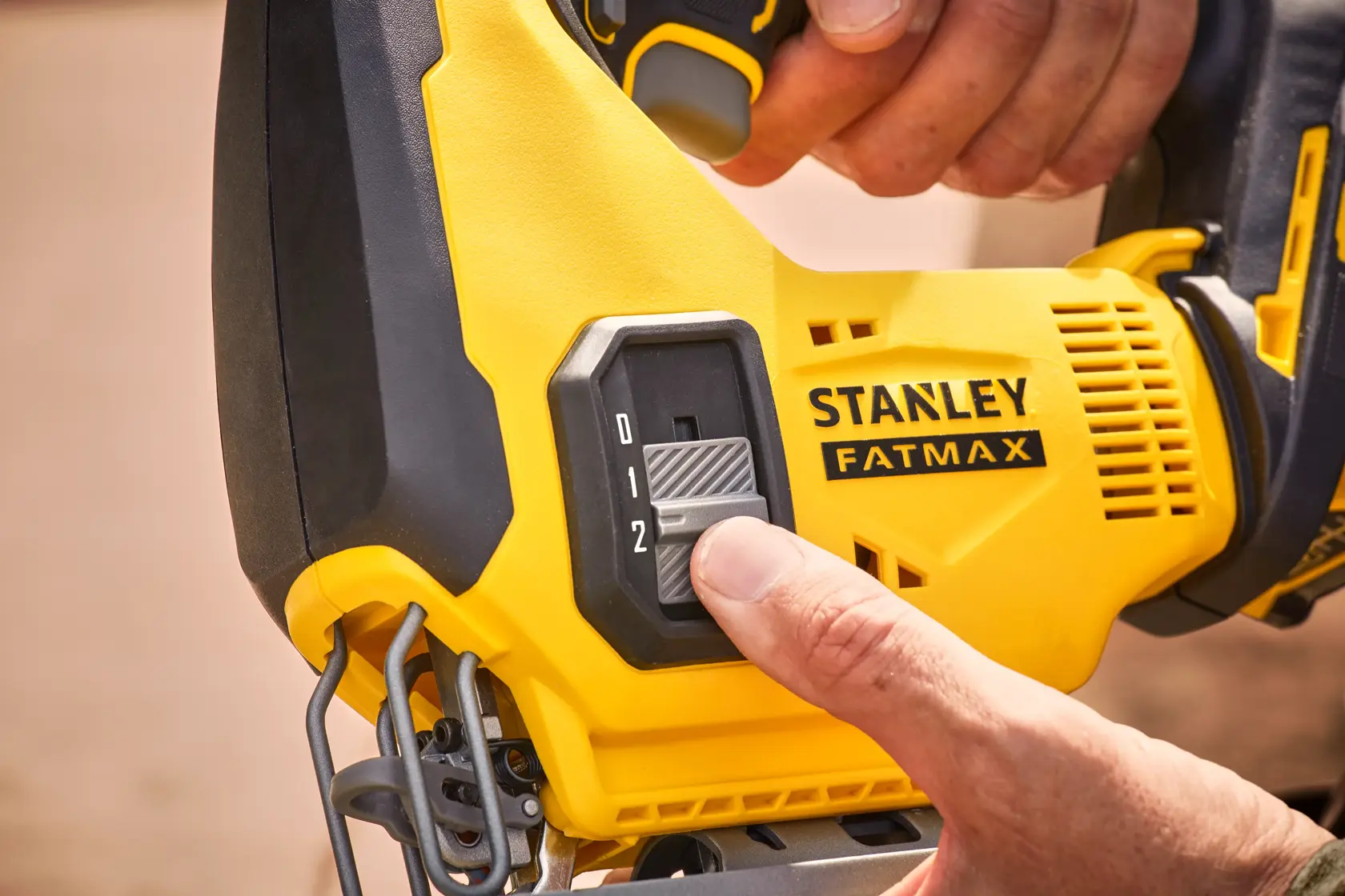 STANLEY SFMCS600B jigsaw close-up, showing hand adjusting speed control switch on yellow and black body.