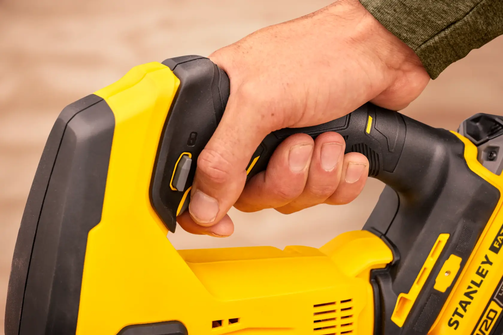 Photo of a hand gripping a STANLEY SFMCS600B cordless saw handle, close-up on black and yellow tool.