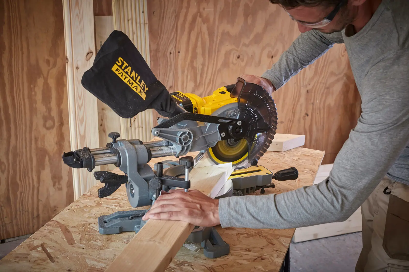 Photo of STANLEY SFMCS701B miter saw cutting wood on a workbench in a workshop setting.