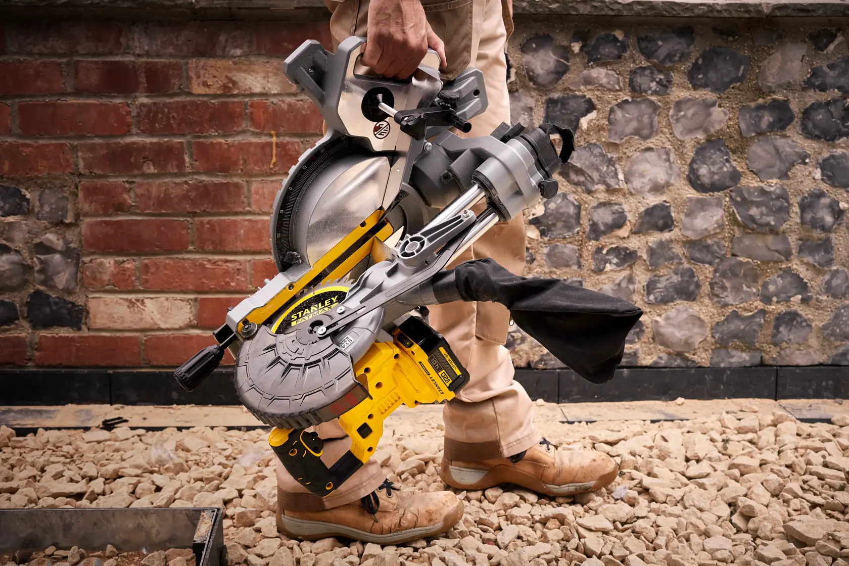 STANLEY SFMCS701M1 miter saw in yellow and silver, carried by hand on construction site.
