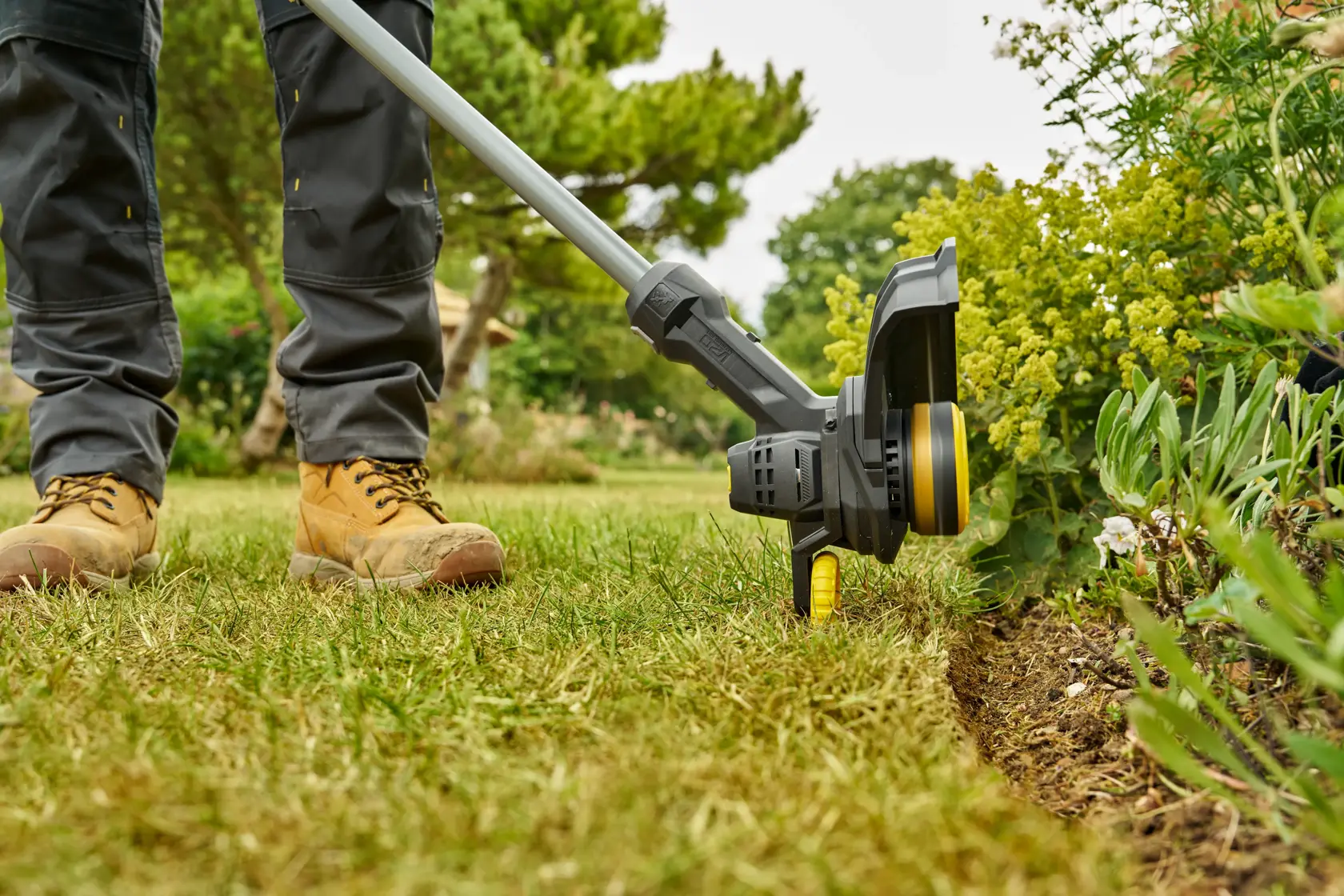 STANLEY SFMCST925M1 grass trimmer in use trimming lawn edge, close-up outdoor view.