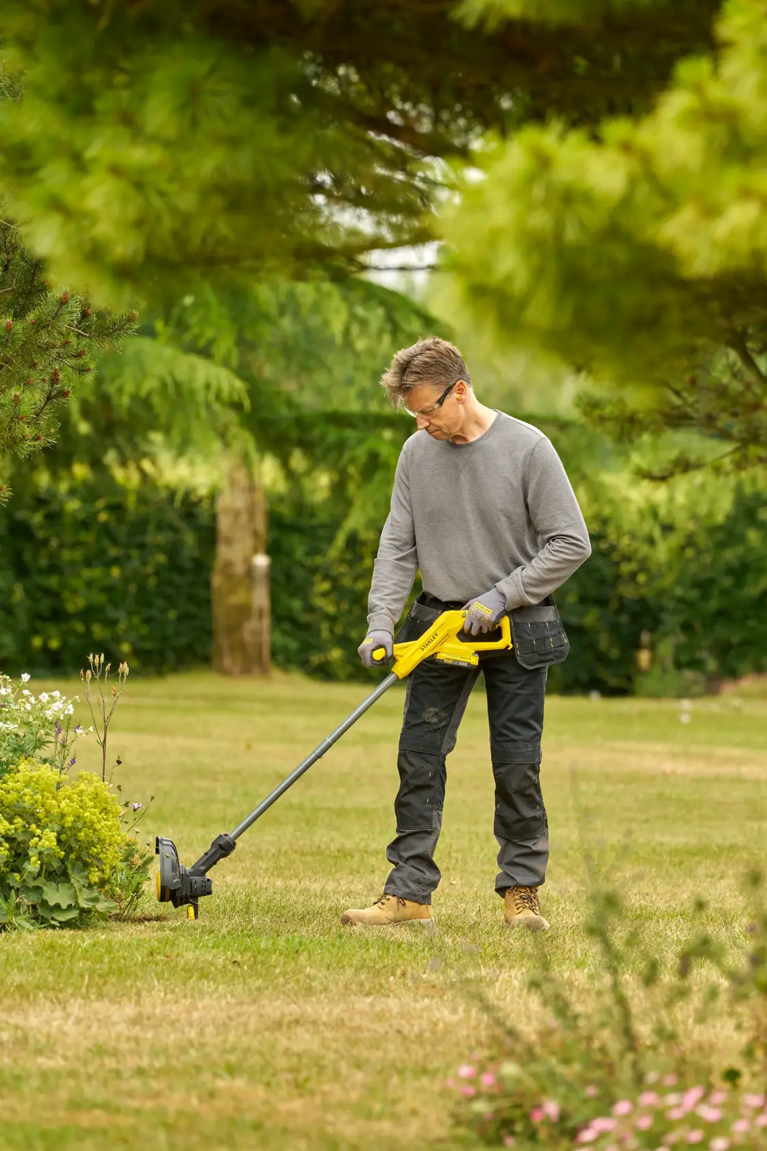 STANLEY SFMCST925M1 yellow cordless grass trimmer in use outdoors on lawn, product photography.