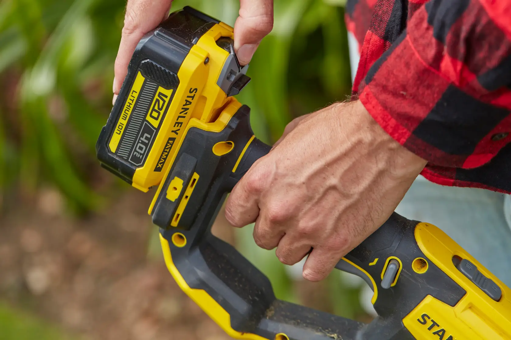 STANLEY SFMCST933B cordless tool close-up, person inserting V20 4.0Ah lithium-ion battery outdoors.