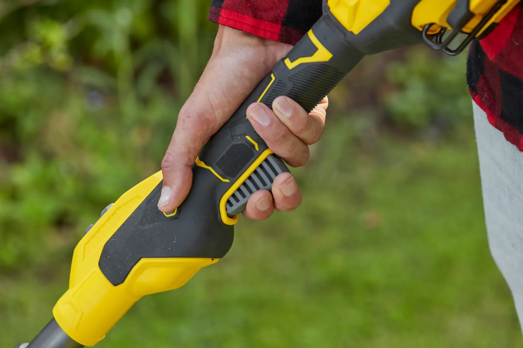 Close-up photo of a hand holding the STANLEY SFMCSTB933B grass trimmer handle, black and yellow design, outdoor use.