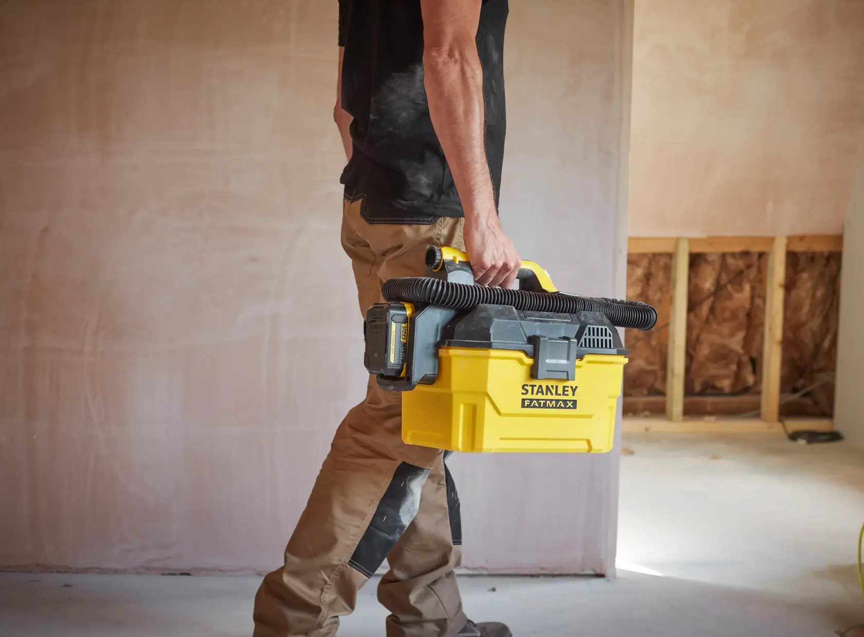 Person carrying STANLEY SFMCV002B portable yellow vacuum with black hose in a construction site.