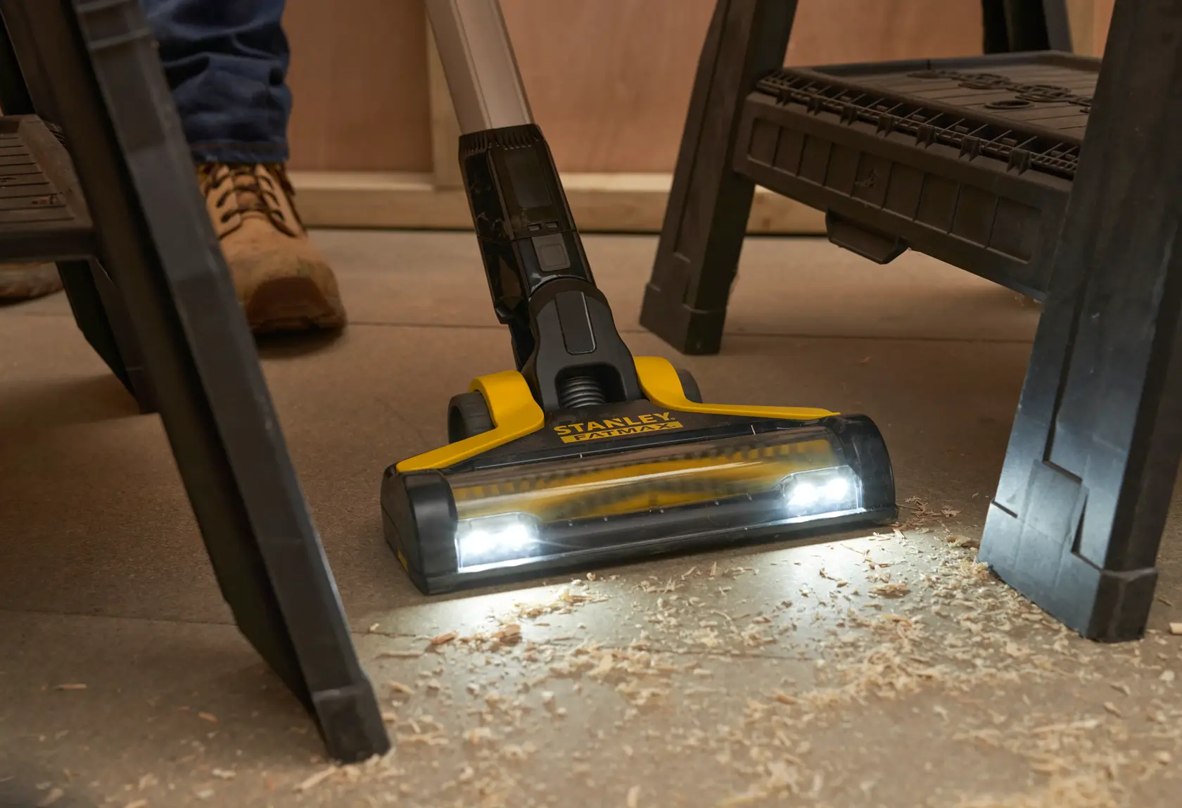 STANLEY SFMCVS001D1 cordless stick vacuum with LED lights cleaning wood shavings under a workbench, front angle.
