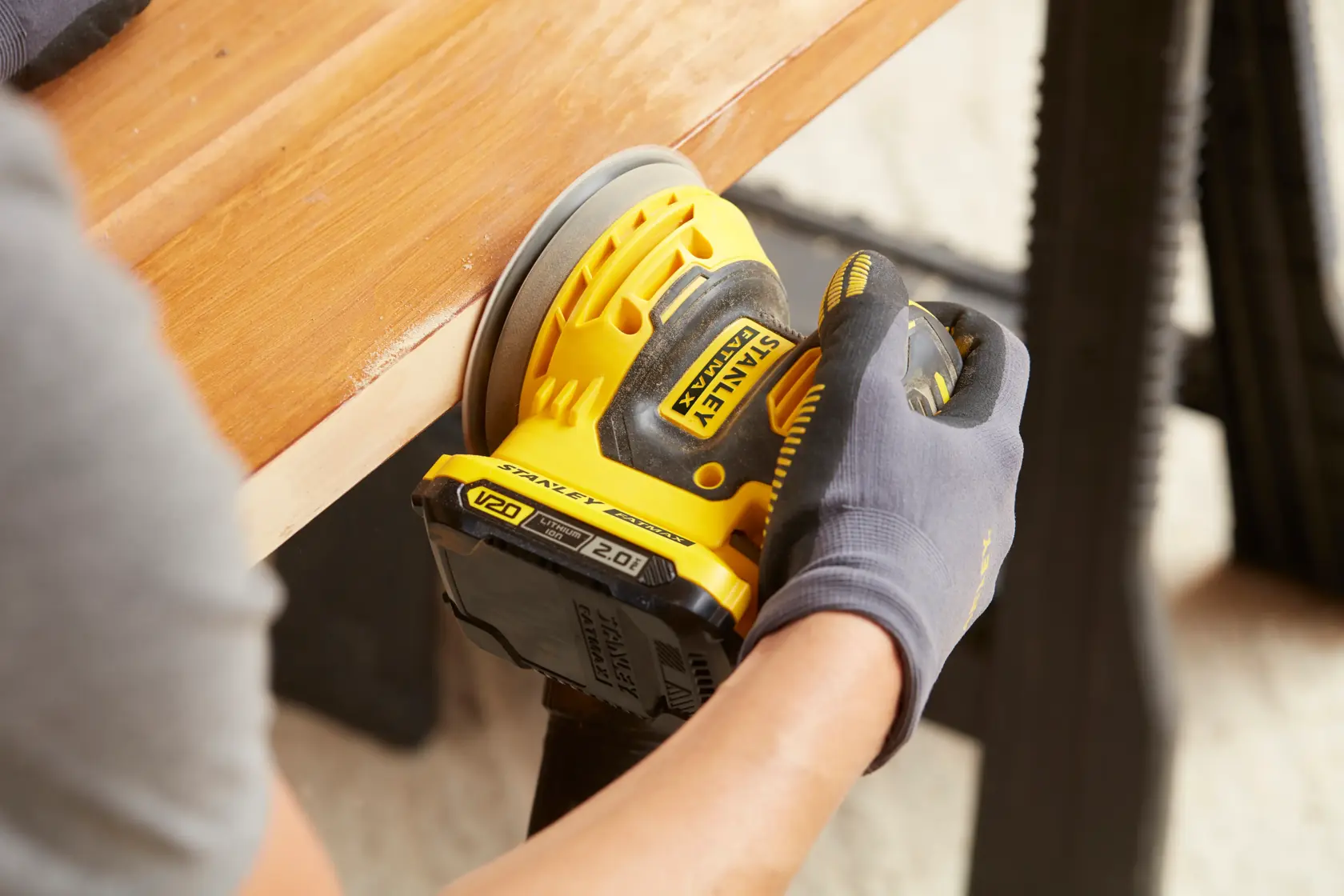 Photo of STANLEY SFMCW220B cordless sander in use on wooden surface, close-up angle.