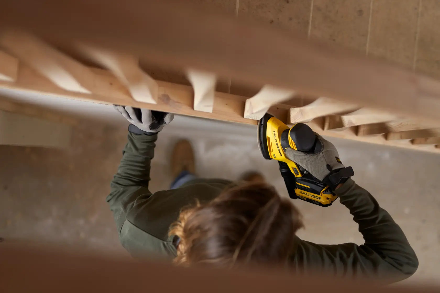Photo of person using STANLEY SFMCW221B cordless sander on wooden staircase railing.