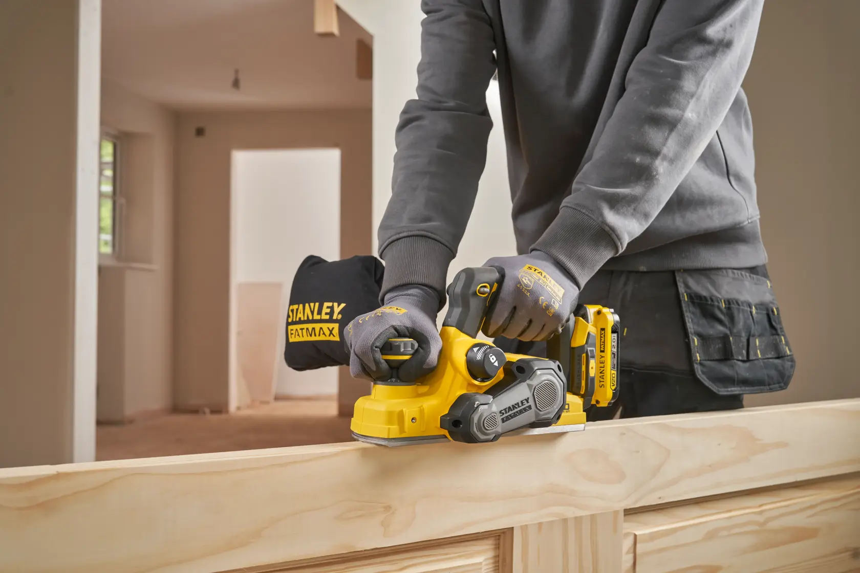 STANLEY SFMCW300B cordless planer in use on wood, operator wearing gloves, indoor workshop setting.