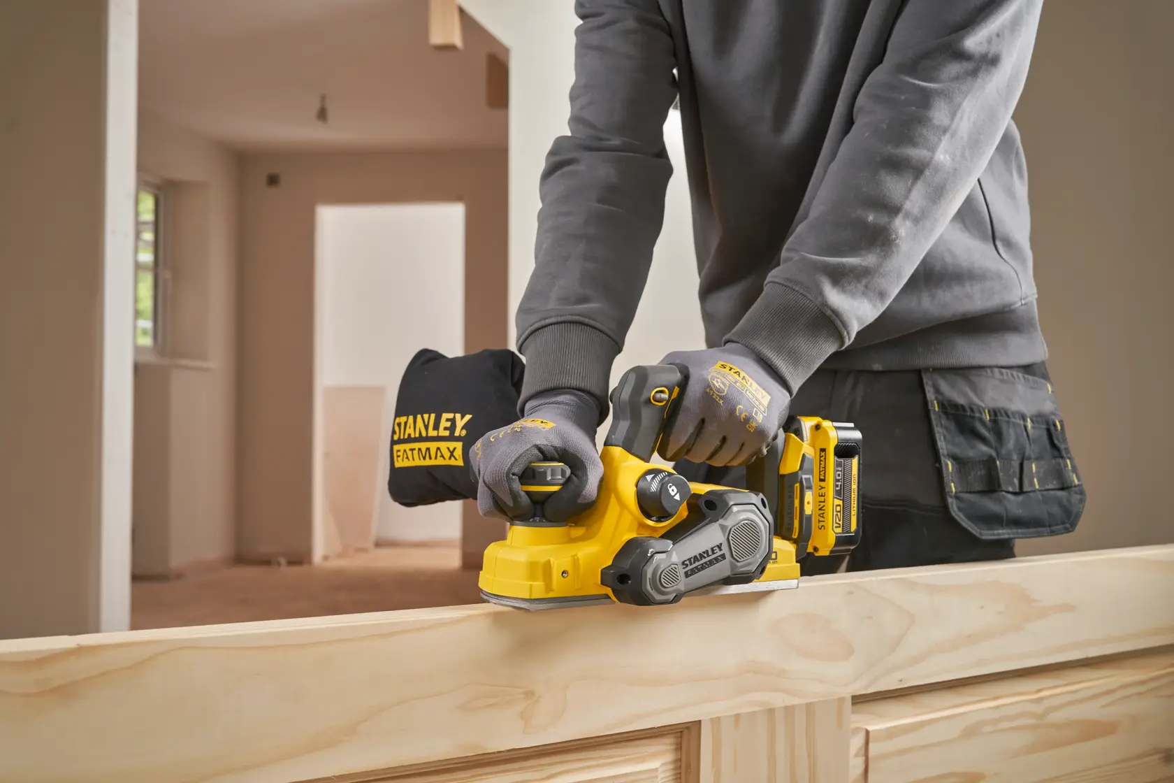 Stanley SFMCW300B cordless planer in use on wood, shown from side angle, worker wearing gloves.
