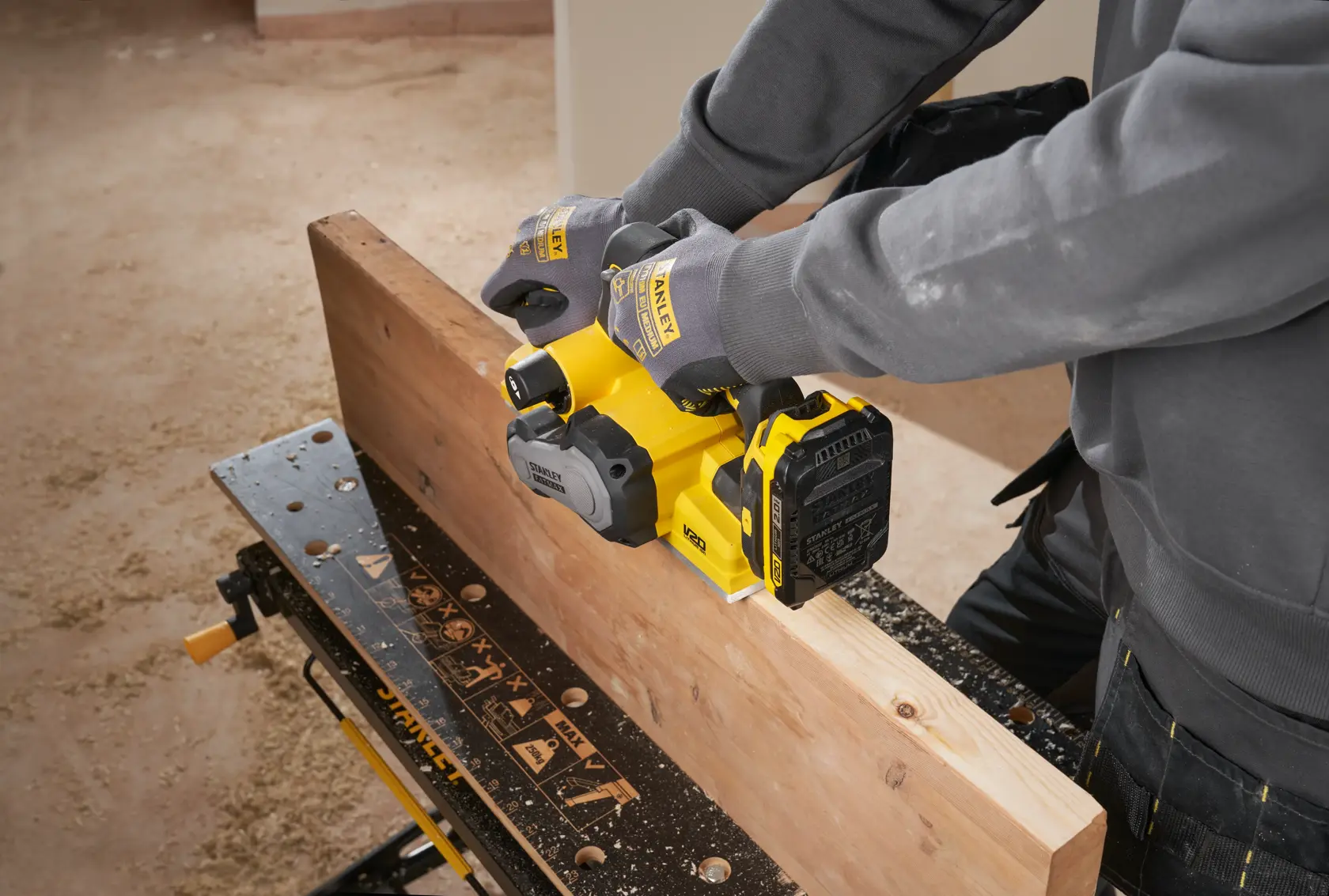 STANLEY SFMCW300B cordless planer in use on wooden beam, side angle, user wearing gloves.