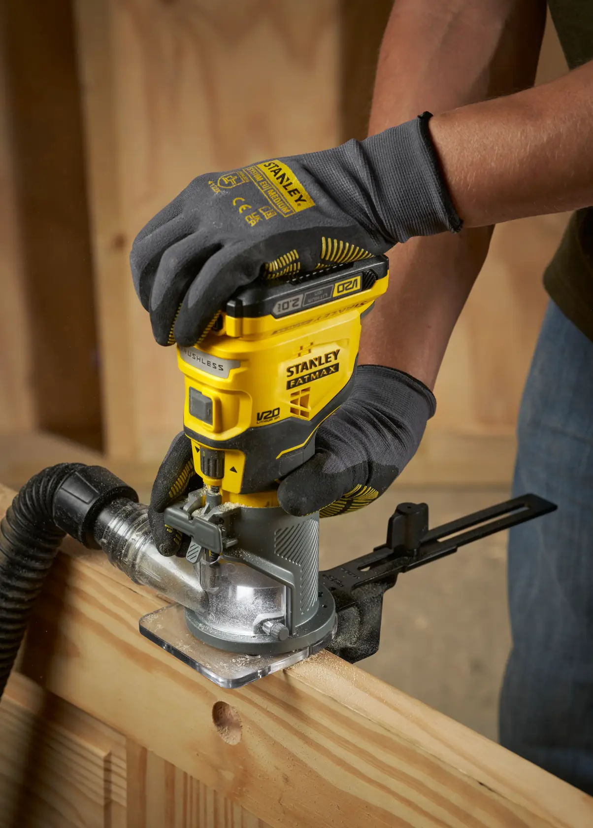 STANLEY SFMCW400B cordless router used on wood by gloved hands, close-up in workshop setting.