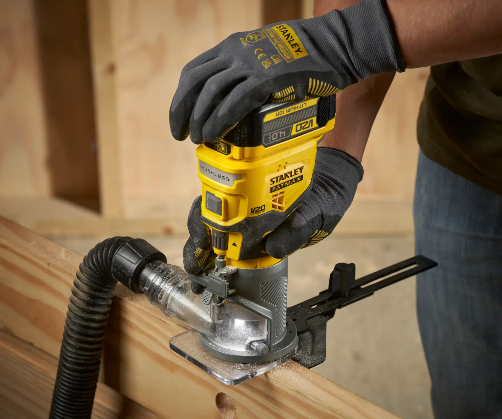 Photo of STANLEY SFMCW400B cordless wood router in use on timber, close-up showing yellow tool and dust extraction.