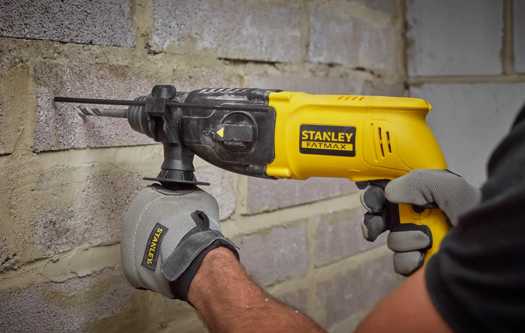 STANLEY SFMEH200K rotary hammer drill in use on masonry wall, yellow and black, close-up photo.