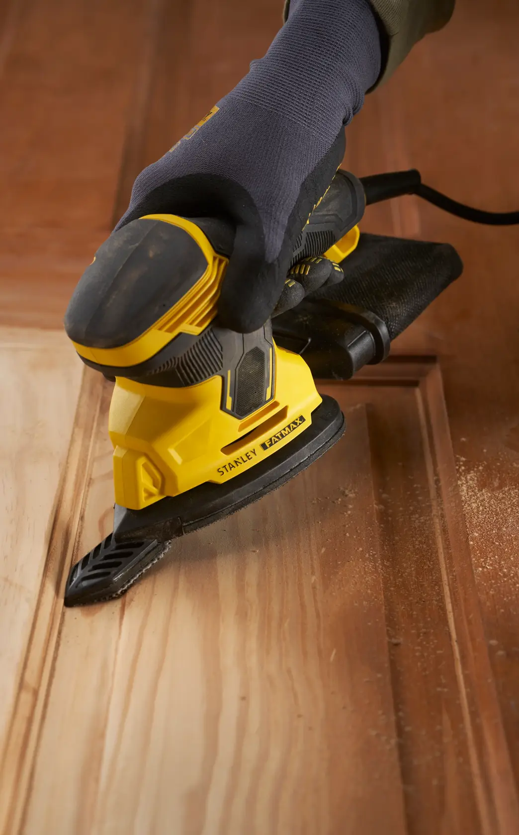 Stanley SFMEW210S sander, yellow and black, in use on wood, close-up at an angle.