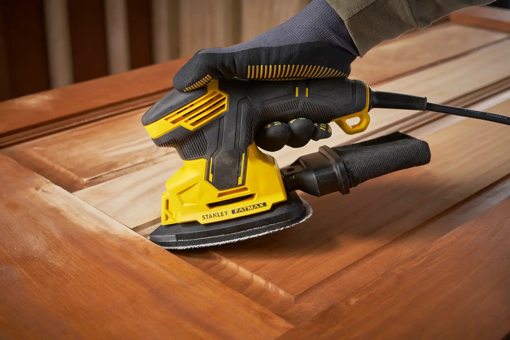 Stanley SFMEW210S sander used on wood surface, close-up, yellow and black design, power tool photography.