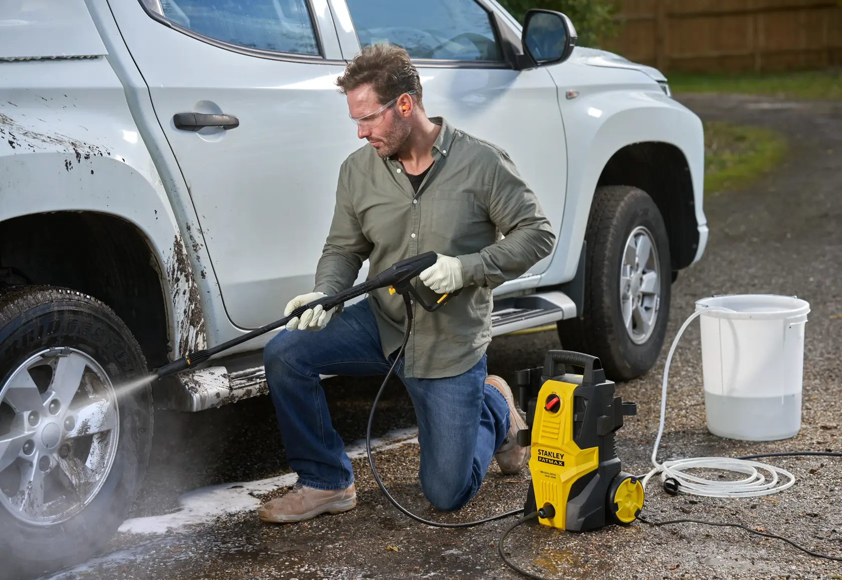 STANLEY SFMPW1740 pressure washer cleaning a white truck wheel outdoors, yellow and black unit with hose and bucket.