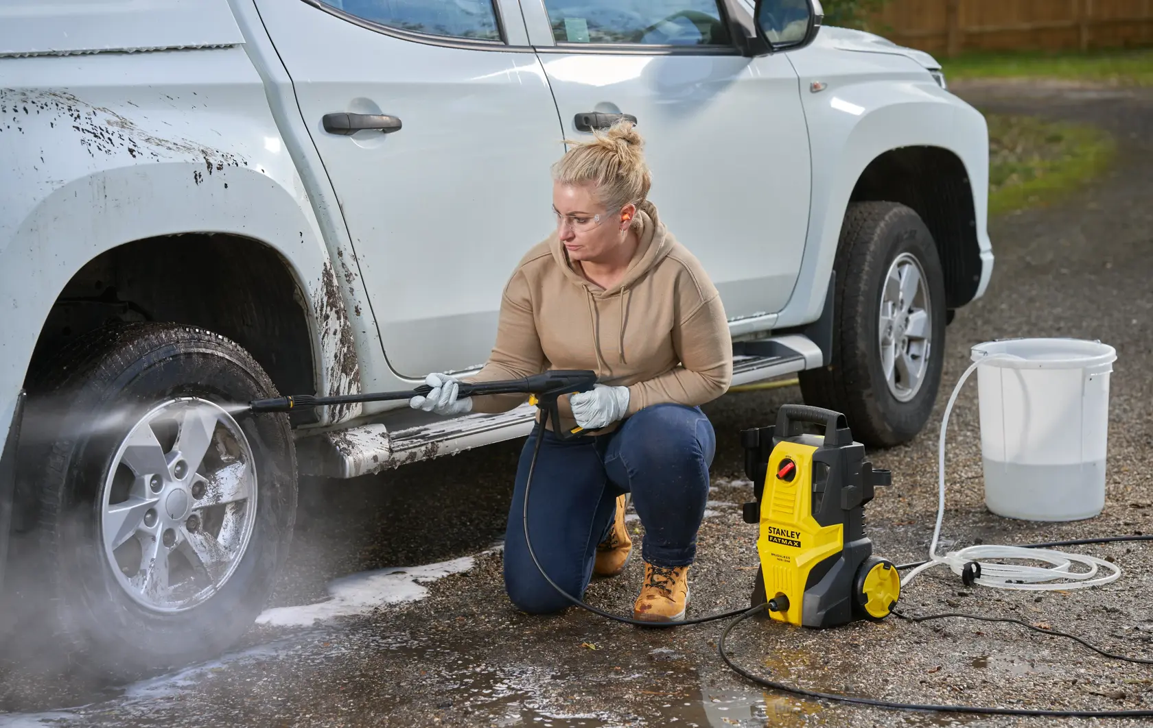 STANLEY SFMPW1740 pressure washer in use cleaning a muddy white pickup truck wheel outdoors.