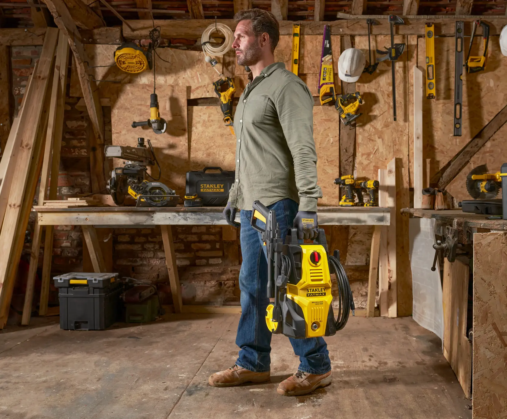 Stanley SFMPW1740 pressure washer held by person in workshop with woodworking tools.