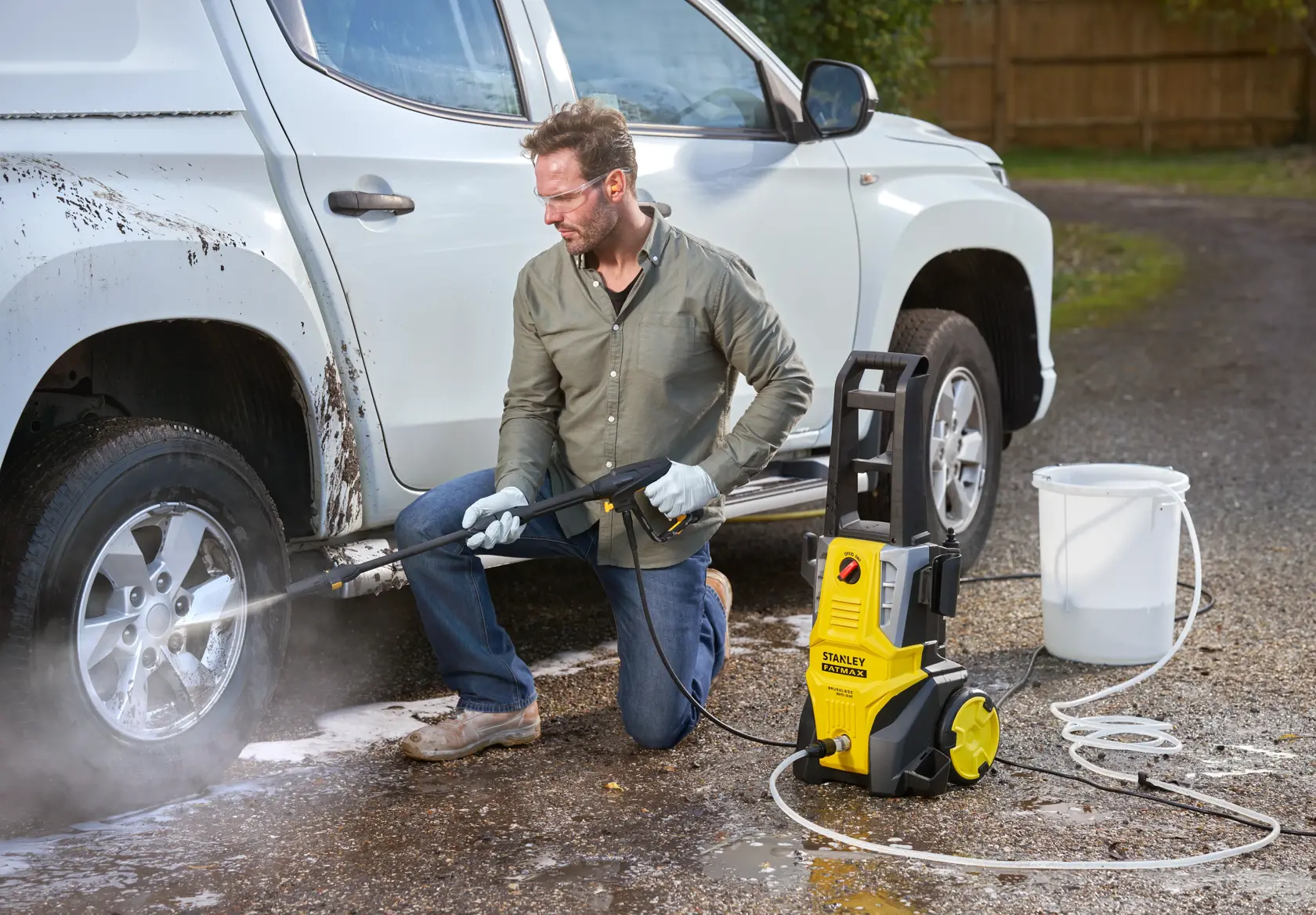 STANLEY SFMPW2000 pressure washer cleaning a white car wheel outdoors, yellow and black unit on ground.