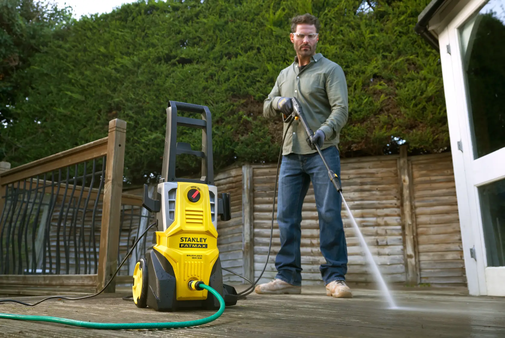 STANLEY SFMPW2000 pressure washer on deck with hose attached, person cleaning wooden surface outdoors.