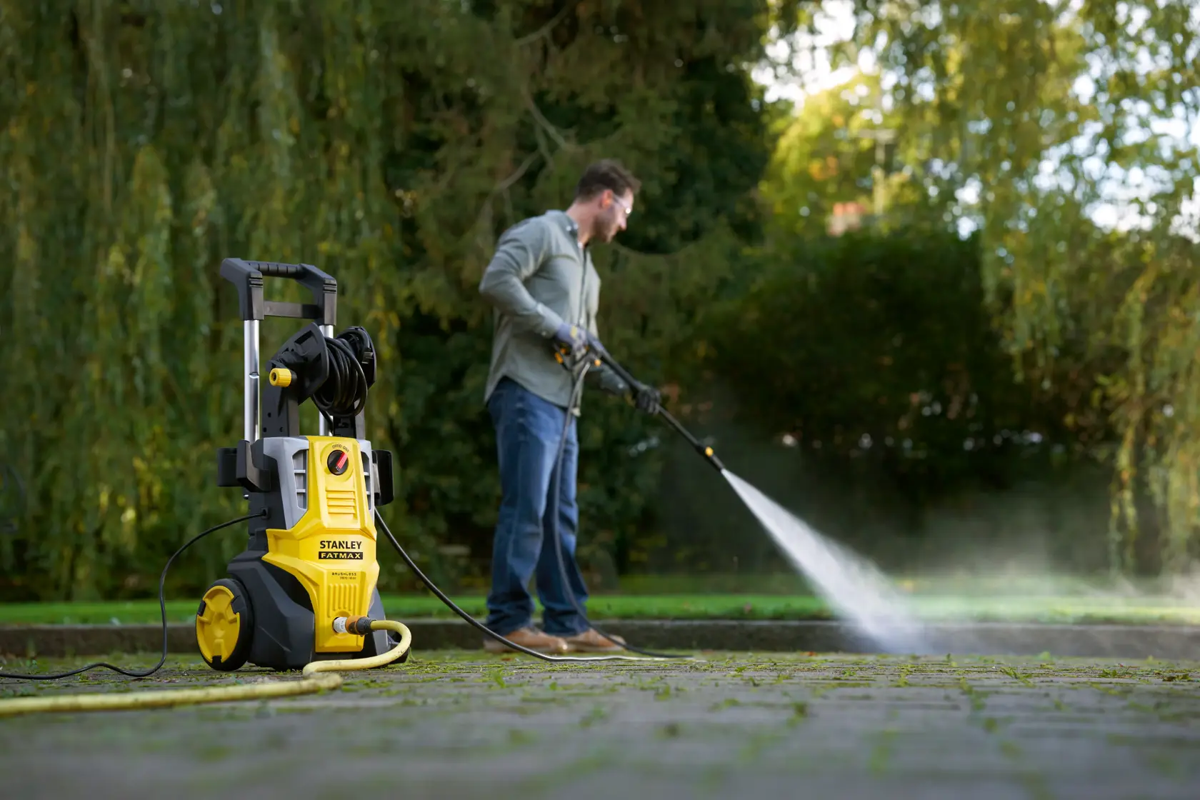 STANLEY SFMPW2400 pressure washer in use outdoors, yellow body, being used to clean paving stones.