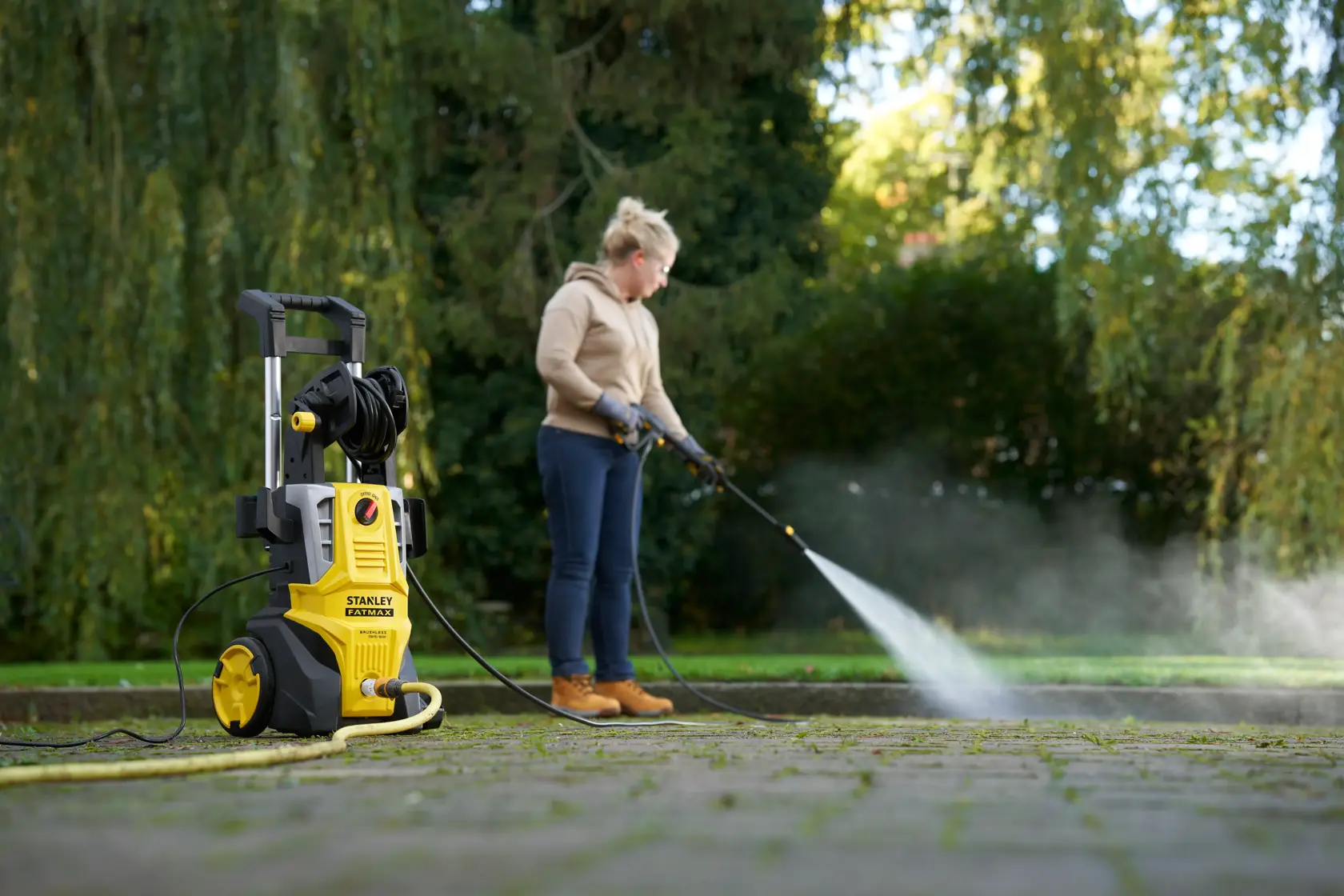STANLEY SFMPW2400 pressure washer in use cleaning outdoor pavement, yellow and black unit in foreground.