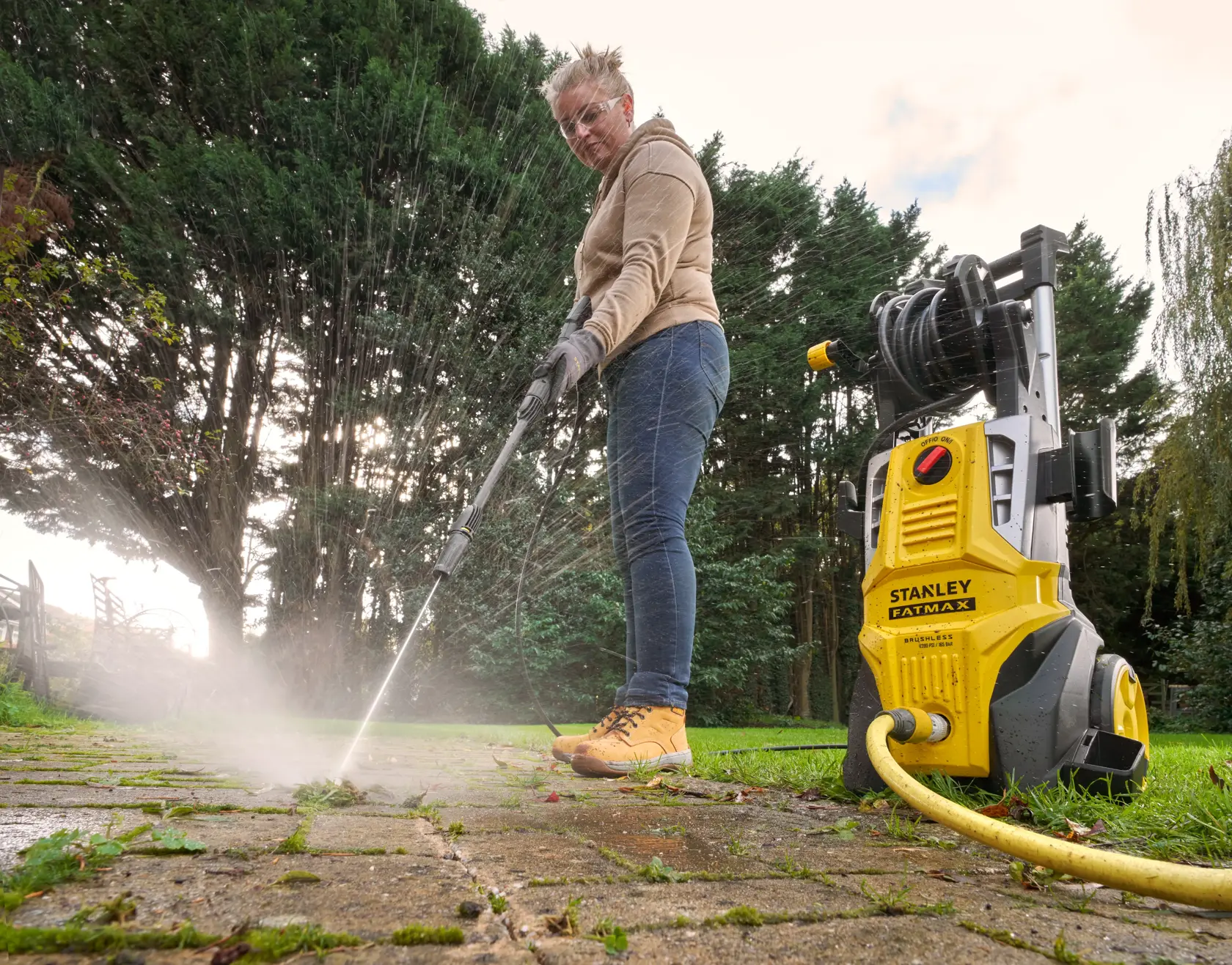 STANLEY SFMPW2400 pressure washer in use outdoors cleaning patio, yellow unit visible on ground.
