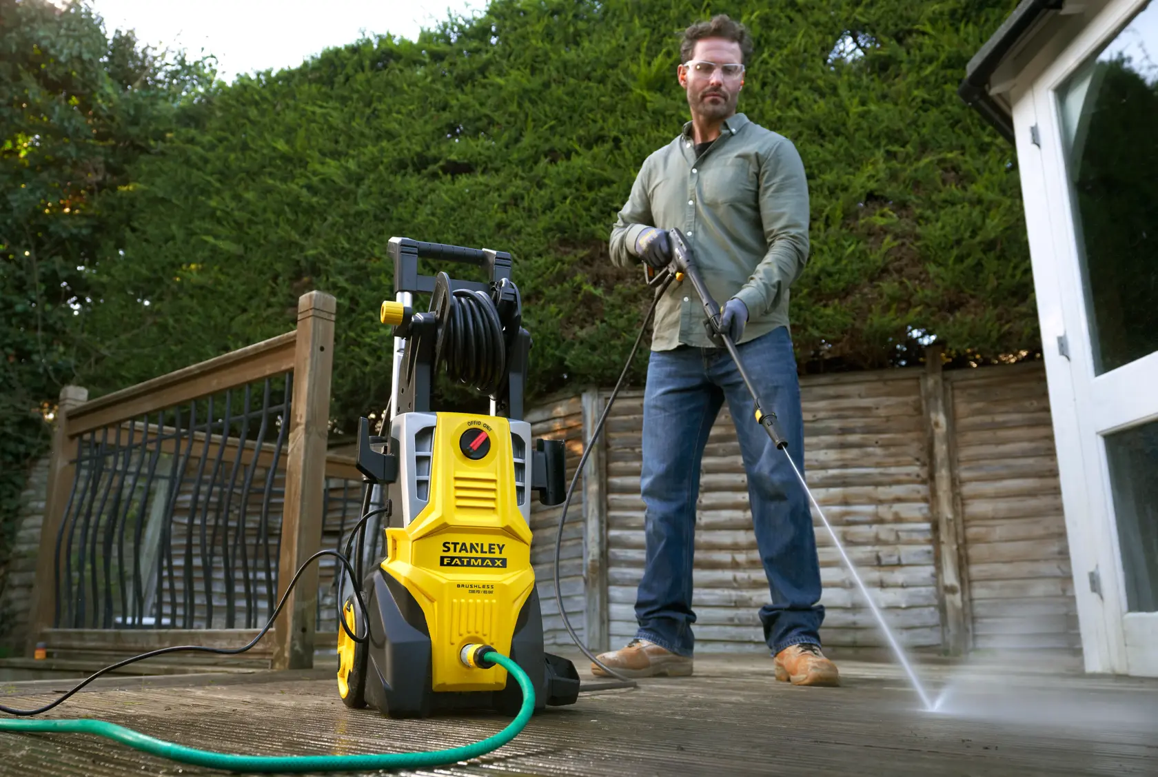 STANLEY SFMPW2400 pressure washer in use outdoors by a person cleaning a wooden deck.