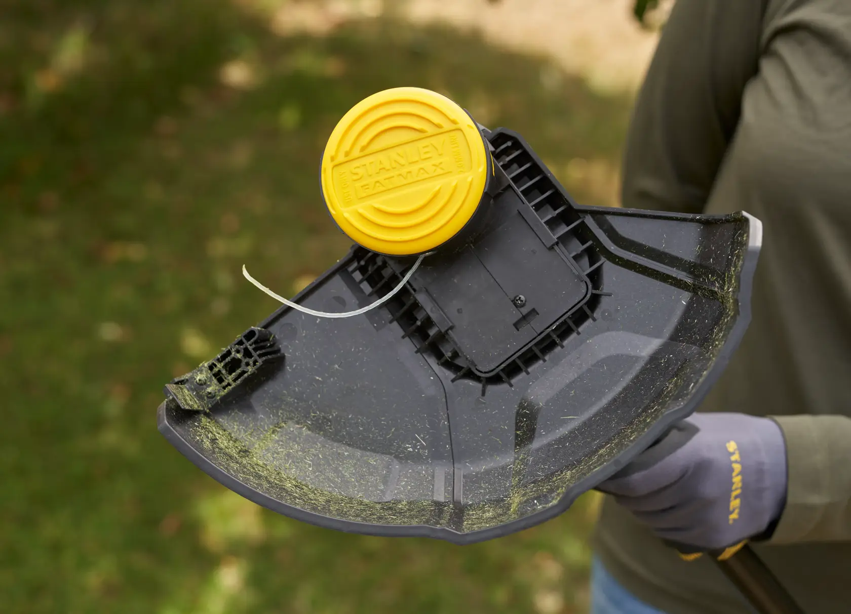 Photo of STANLEY SFMSTB930M grass trimmer head with yellow cap and black shield, shown outdoors in use.