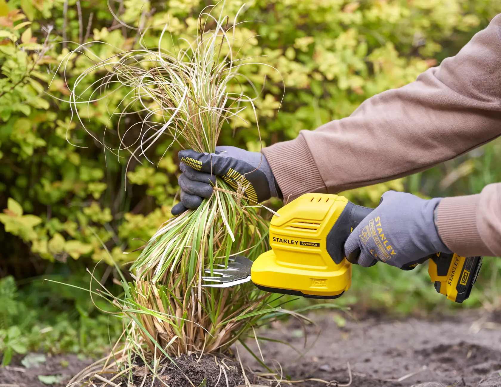 Photo of STANLEY STCSS20B grass shear in use, yellow tool held by gloved hands trimming garden grass.